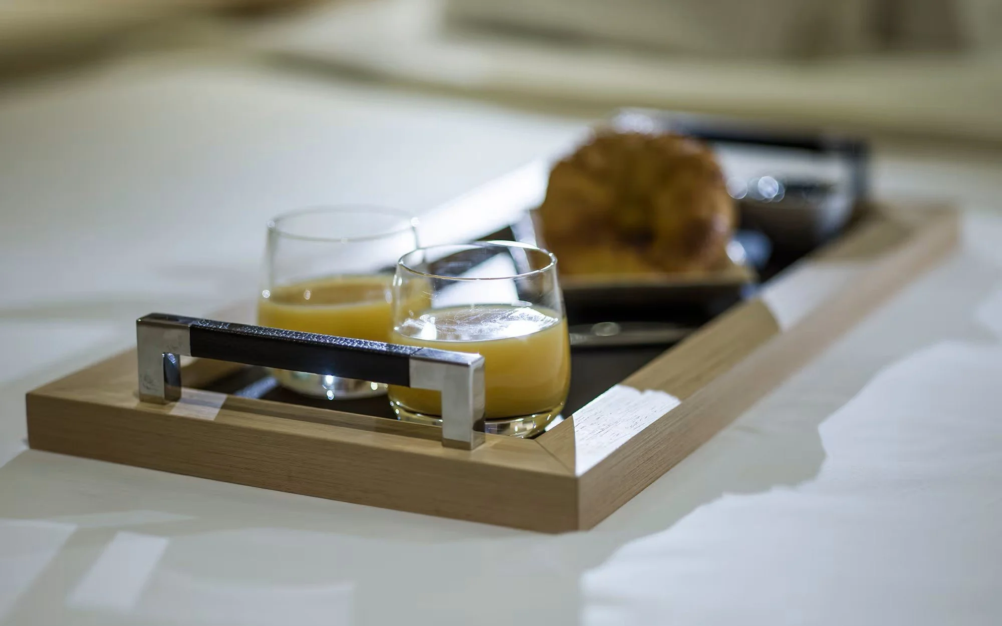 Tray with two glasses of orange juice and a plate of food in the background.