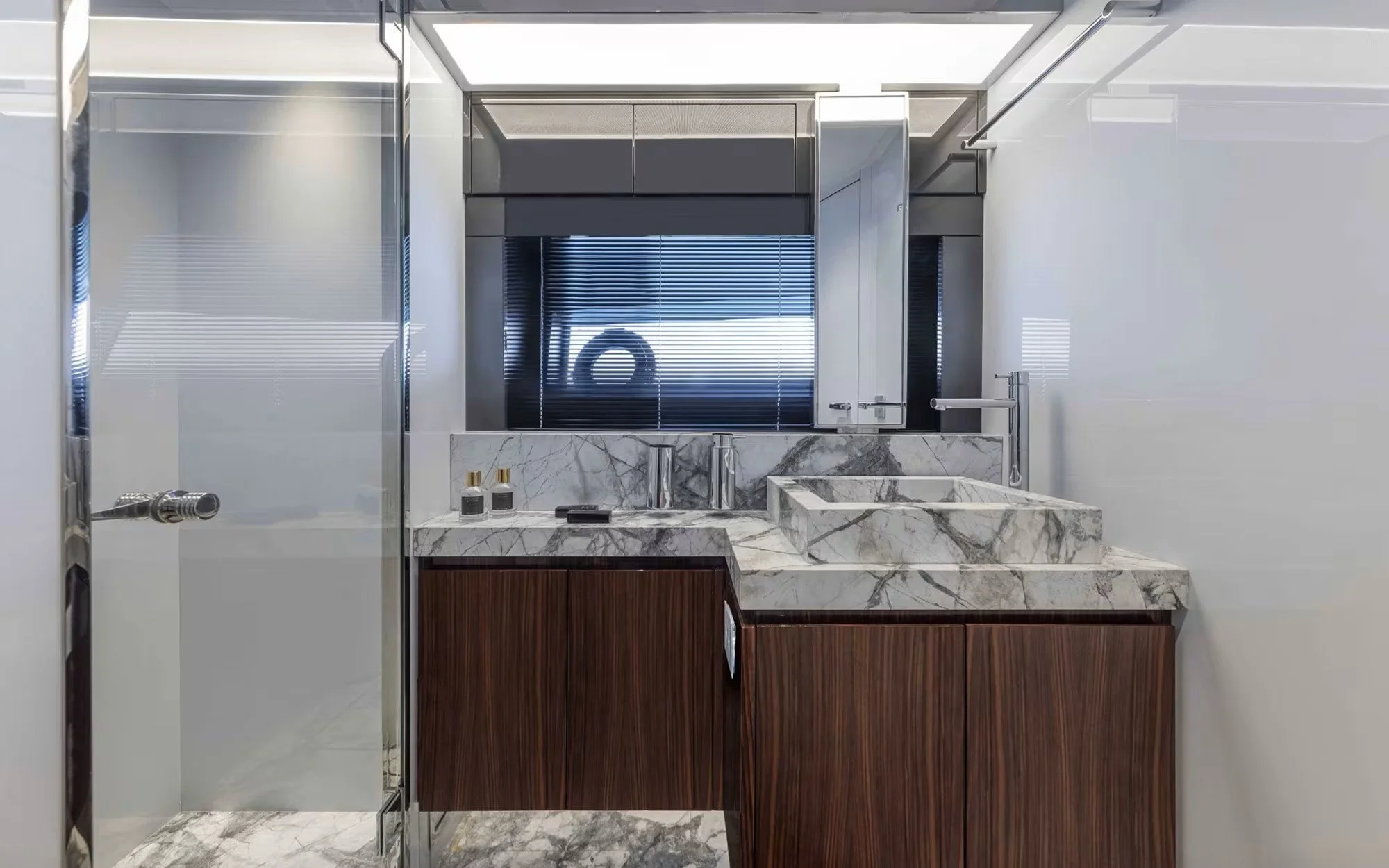 Modern bathroom with marble sink, wooden cabinets, mirror, and glass shower enclosure.