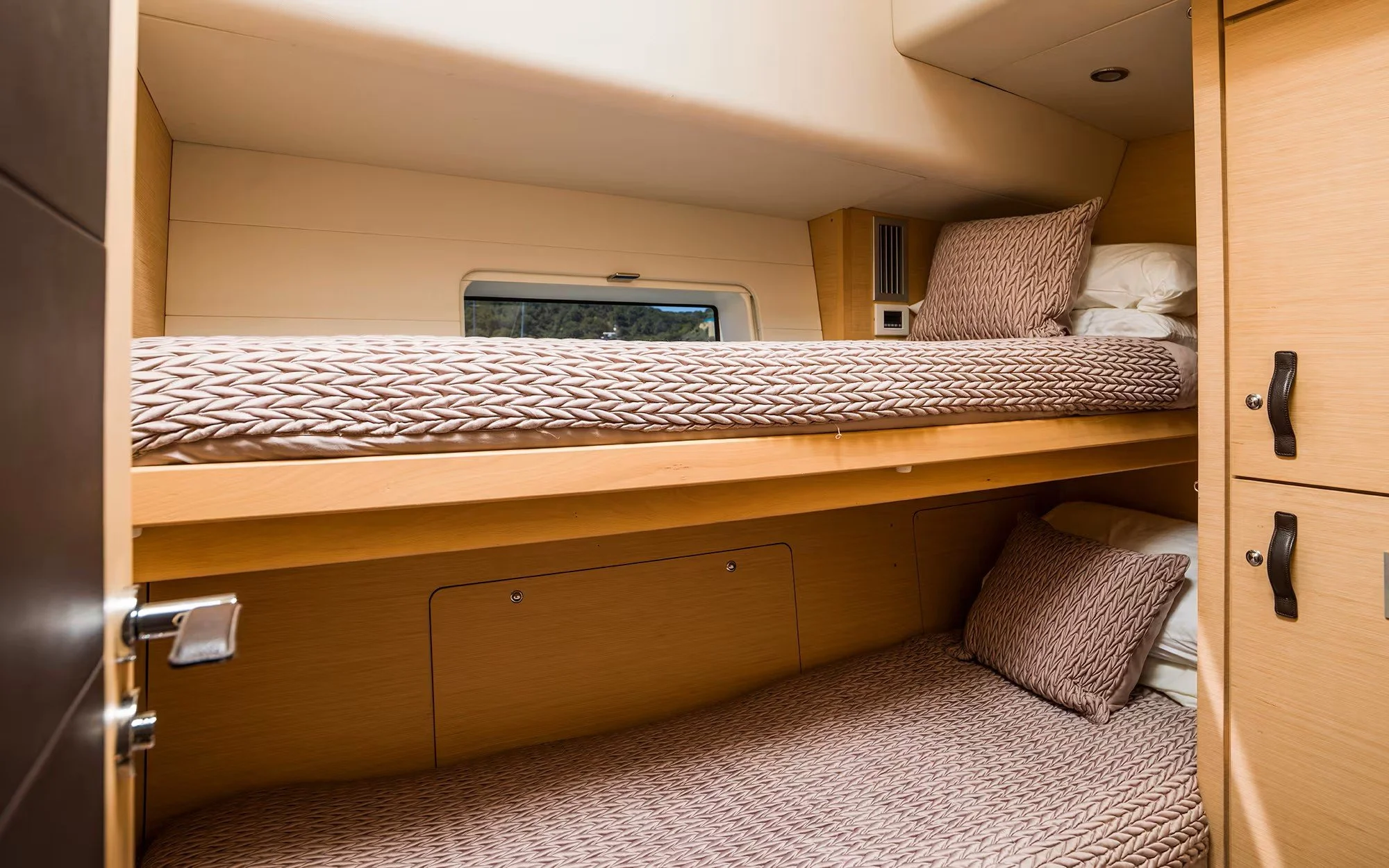 Bunk beds in a compact wooden cabin, with patterned bedding and pillows, small window, and built-in storage.