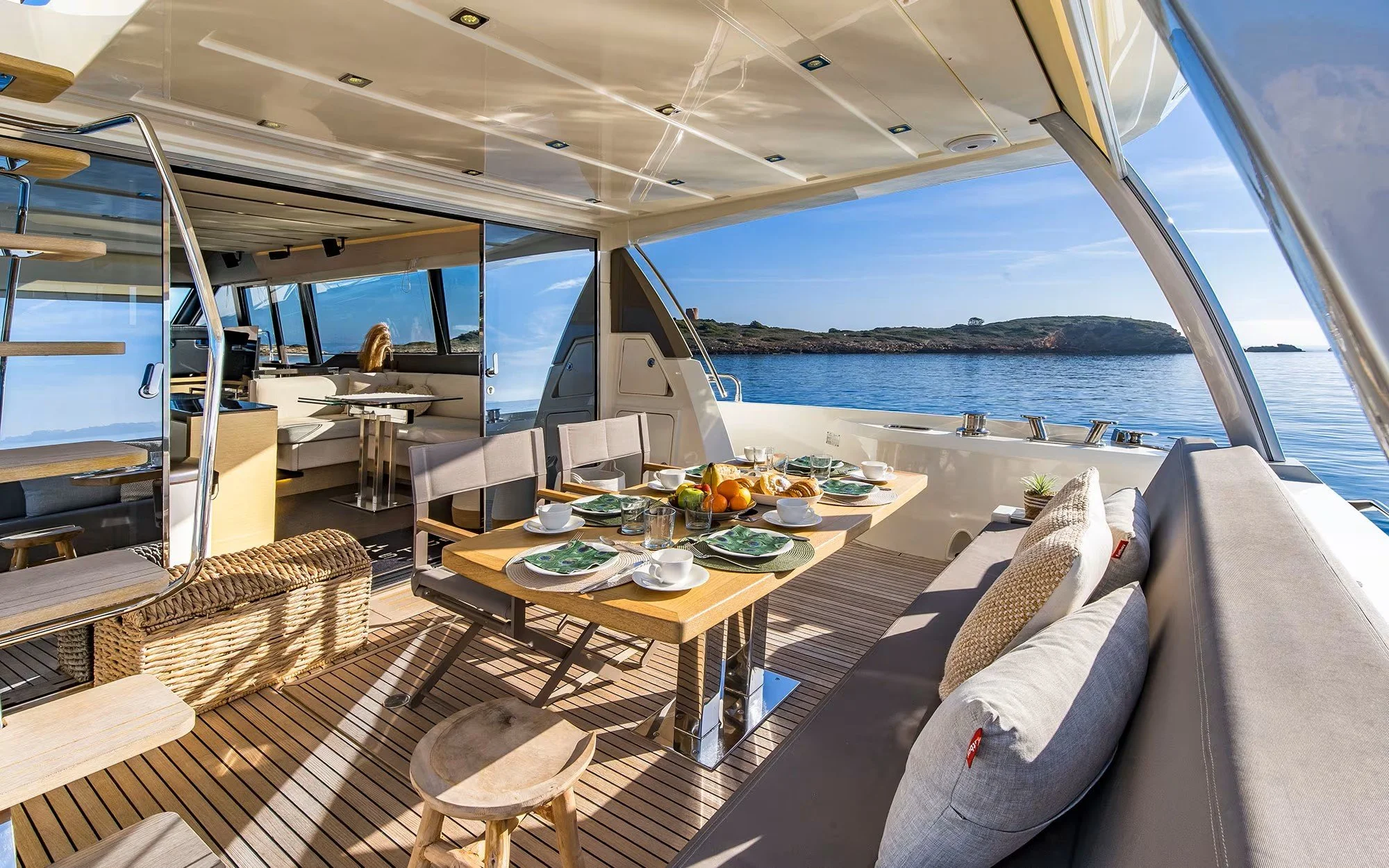 Luxury yacht interior with dining area on the deck, set for breakfast, overlooking the ocean and distant islands.