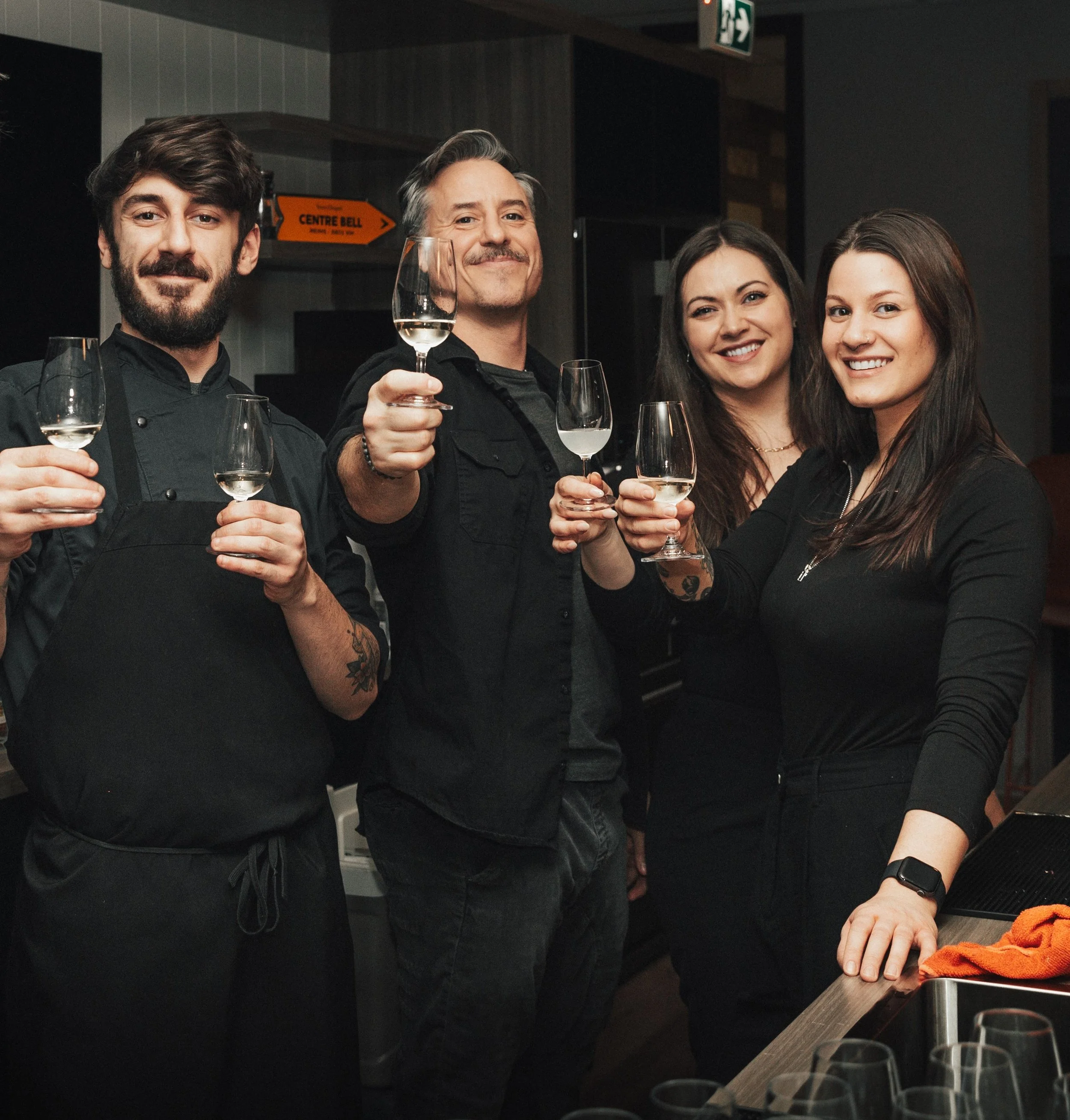 Équipe de service, mixologues et cuisiniers de quatre personnes, deux hommes et deux femmes, en train de faire un toast avec des verres de vin blanc dans événement corporatif.