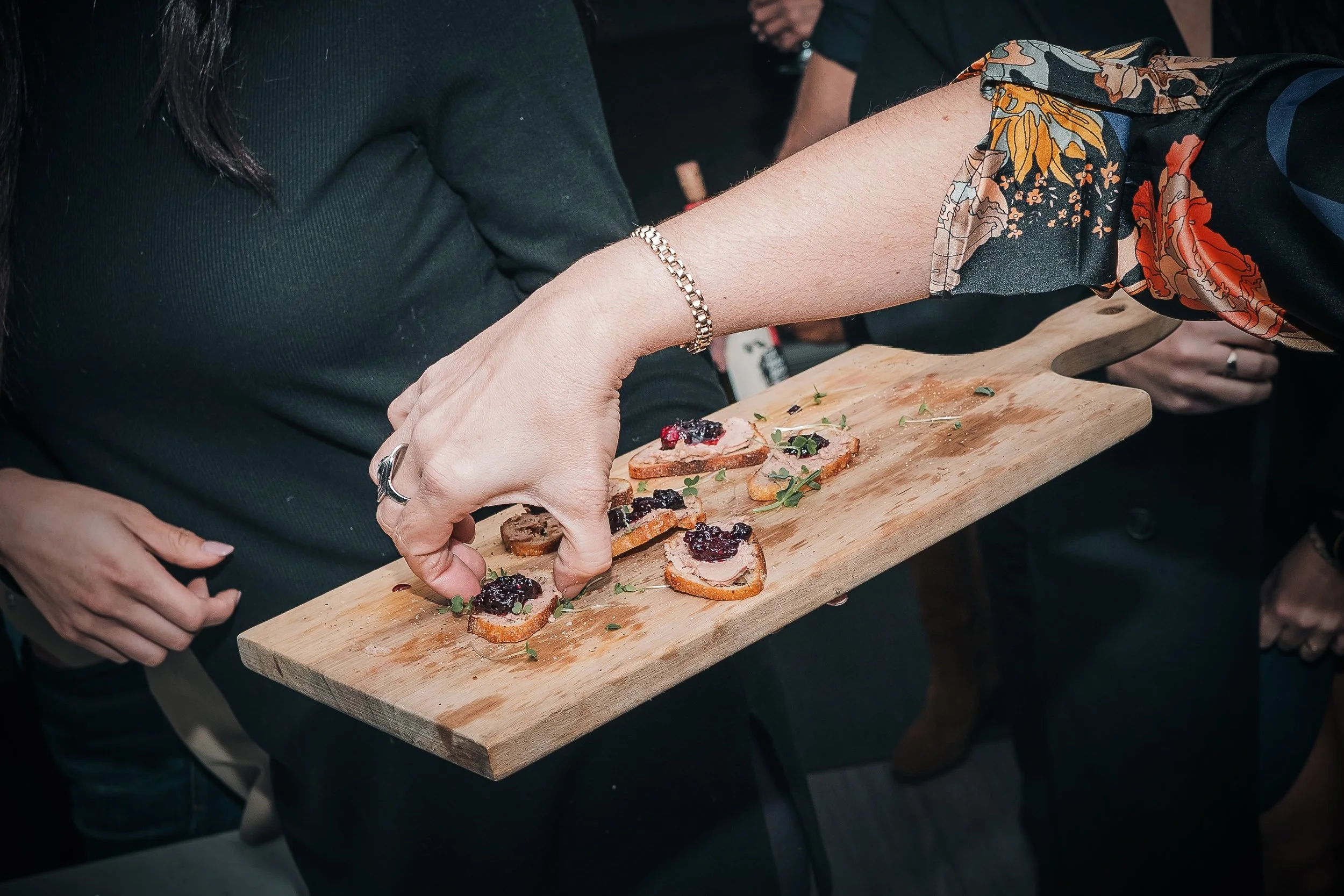 Une personne sert des toasts garnis de confiture ou de compote de fruits sur un plateau en bois lors d'une dégustation ou d'une réception.