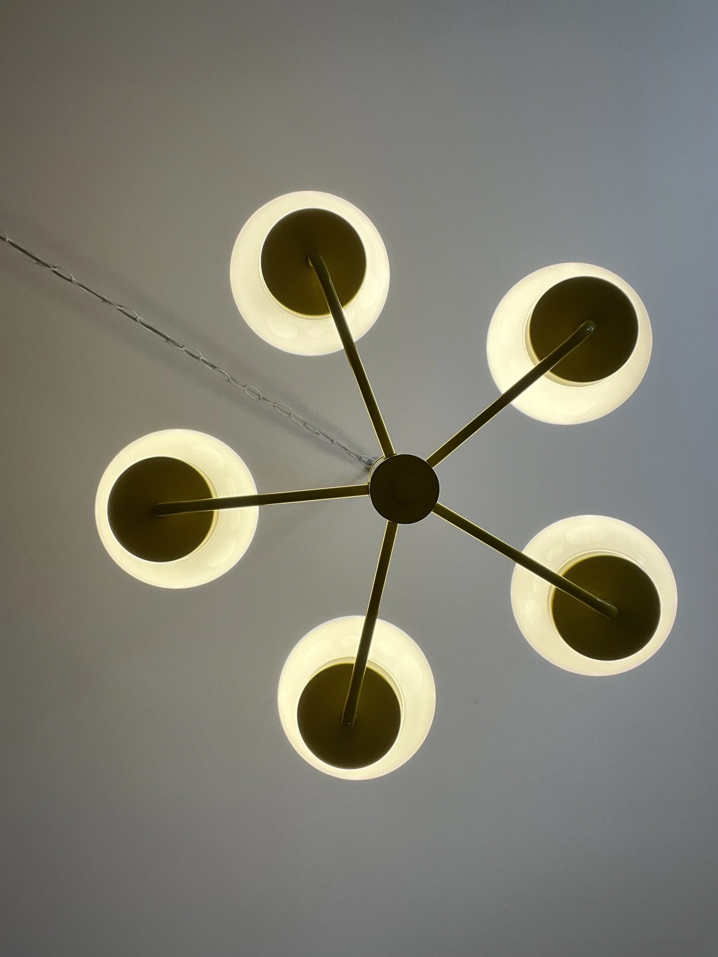 Bottom view of vintage canary yellow chandelier showing five radial metal arms and round white glass globes with lights on.
