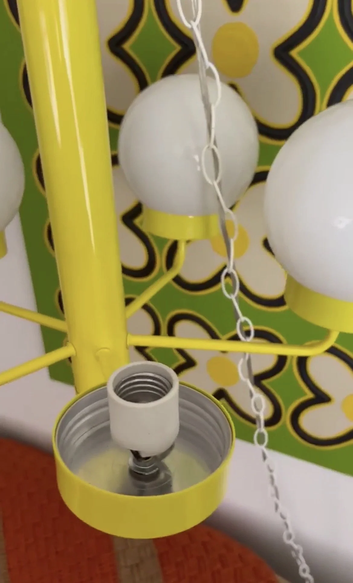 Close-up of yellow metal chandelier frame showing a white lamp socket and threaded fitter used to secure the glass globes.