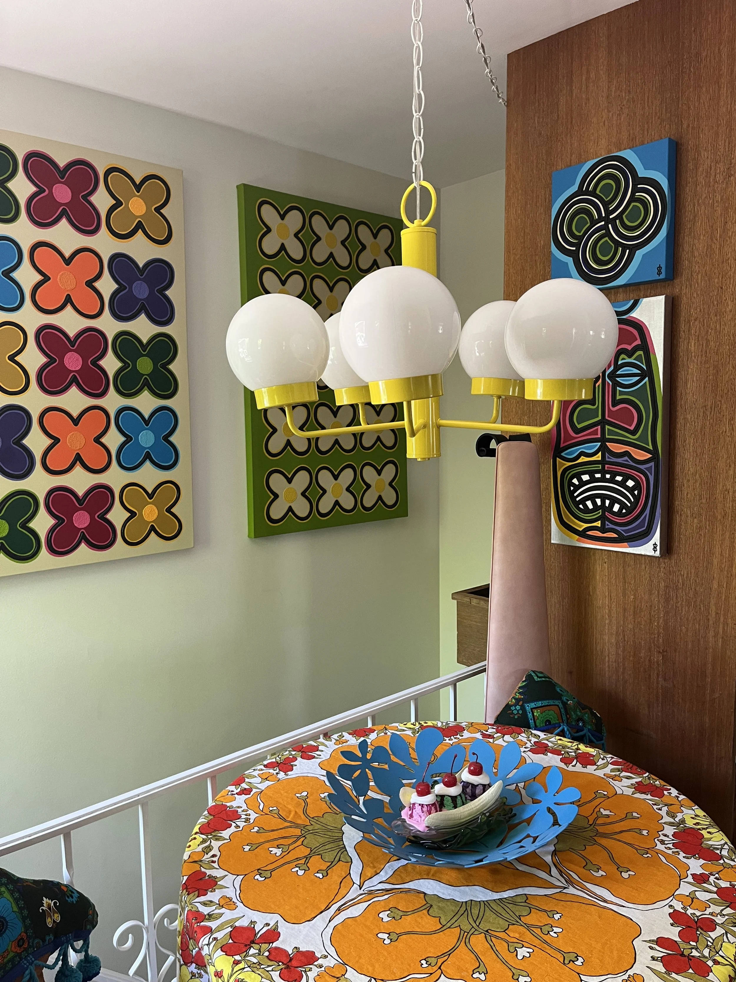Five-arm vintage canary yellow chandelier with round white glass globes hanging in a dining room with retro artwork.