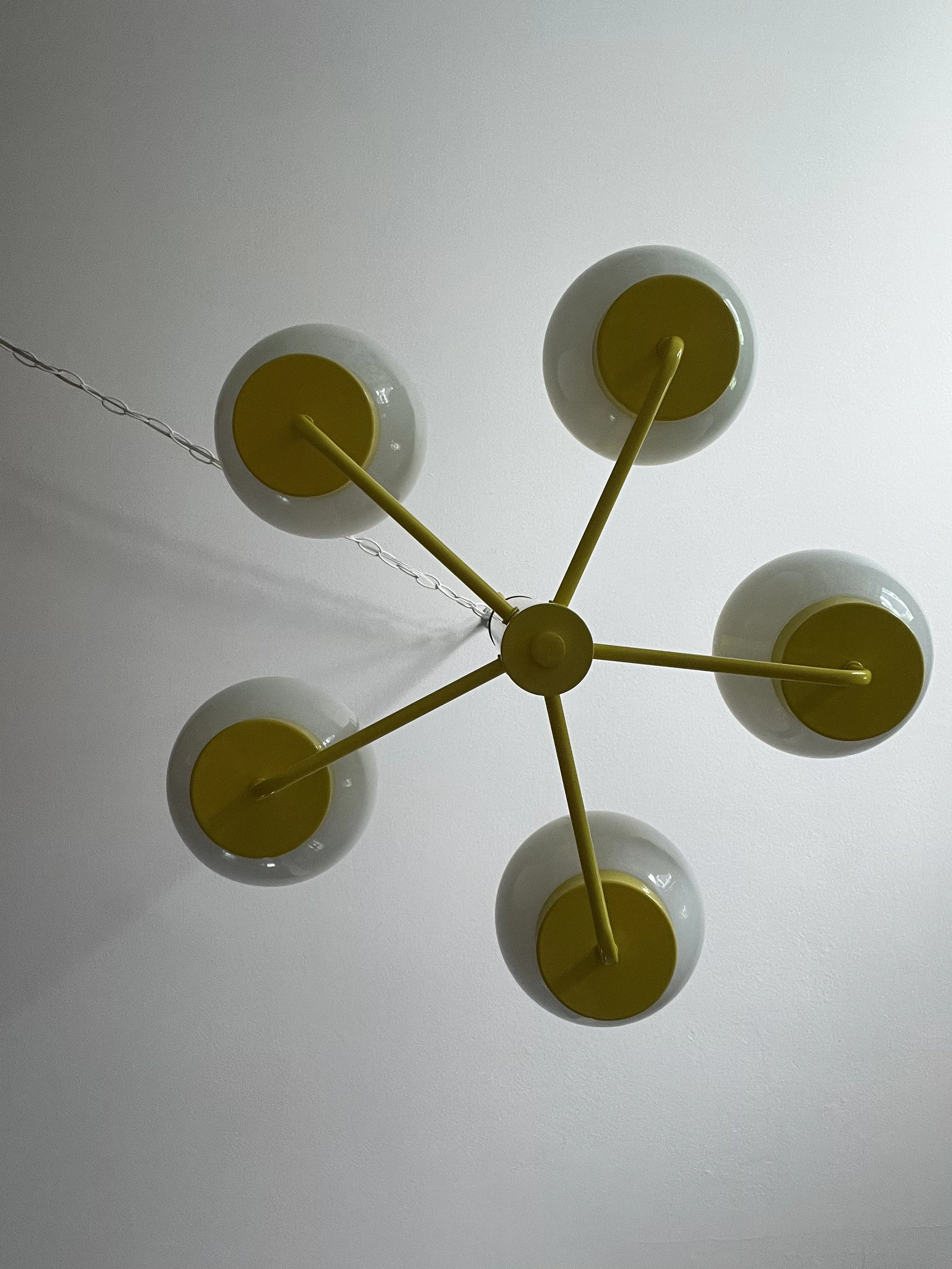 Bottom view of vintage canary yellow chandelier showing five radial metal arms and round white glass globes with lights off.