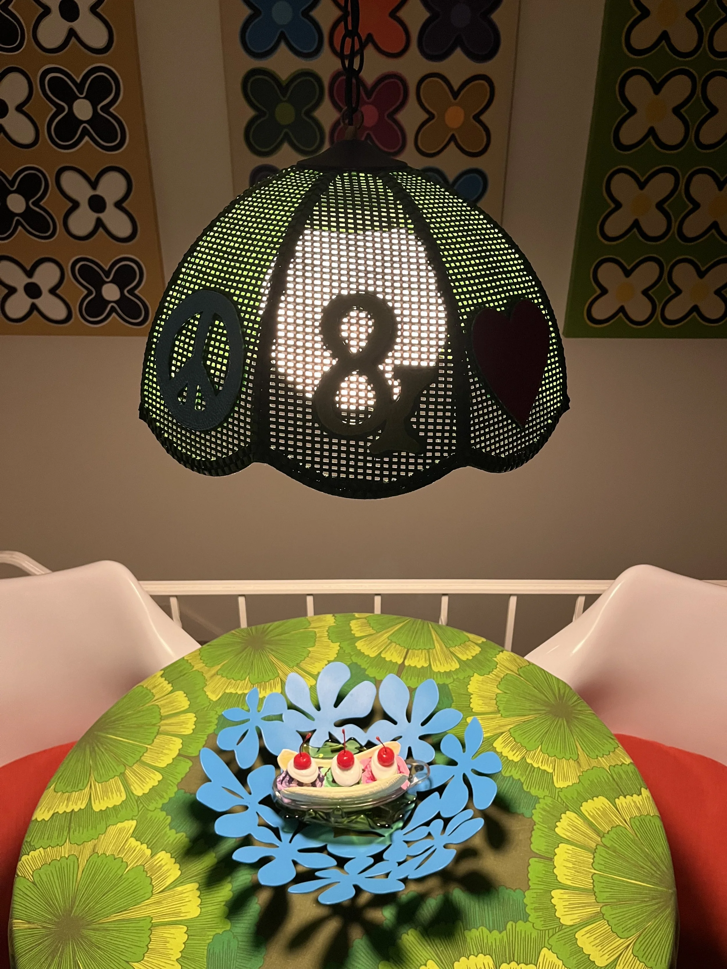 Close-up of the Peace & Love light showing its hand-painted green rattan shade, ampersand, and peace symbols.