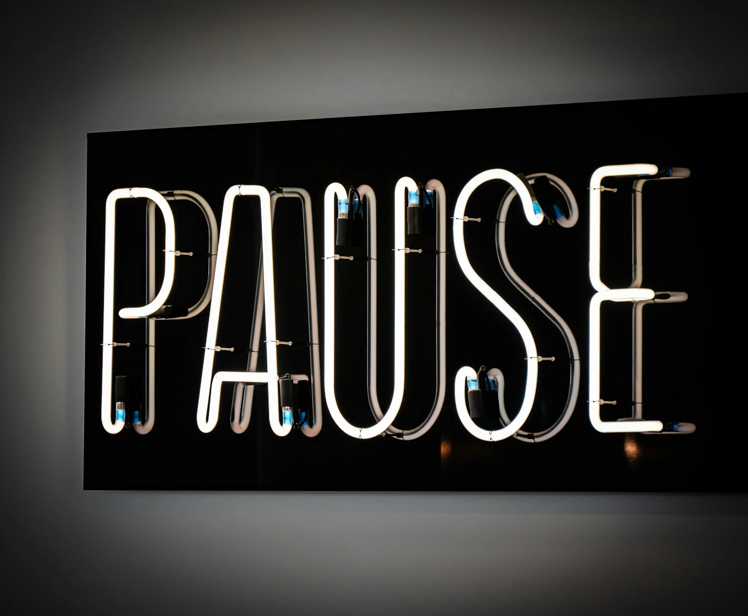 Neon sign displaying the word "Pause" representing the importance of slowing down to prevent stress and burnout.