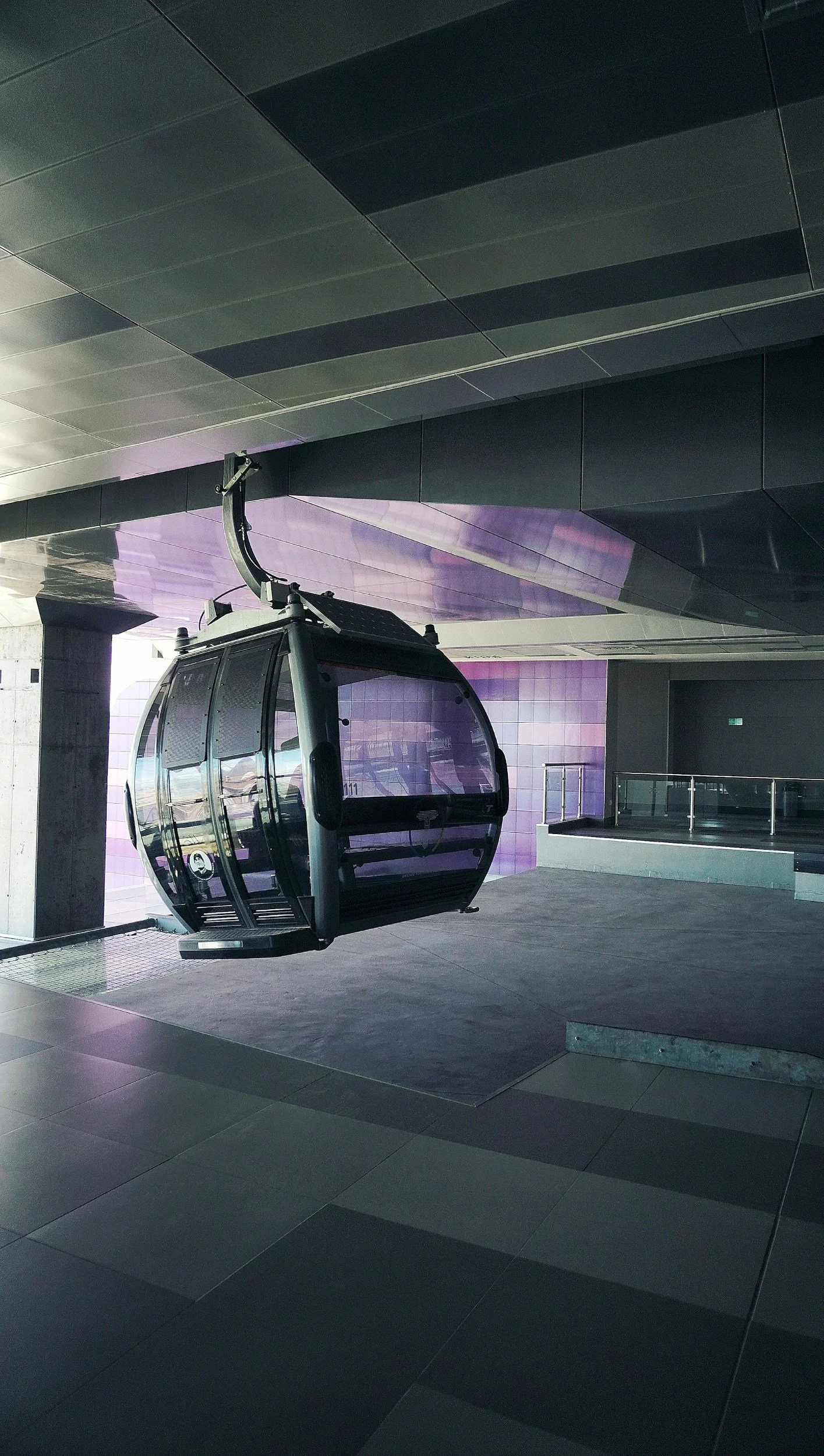Modern gondola lift at a station with reflective windows and a tiled floor.