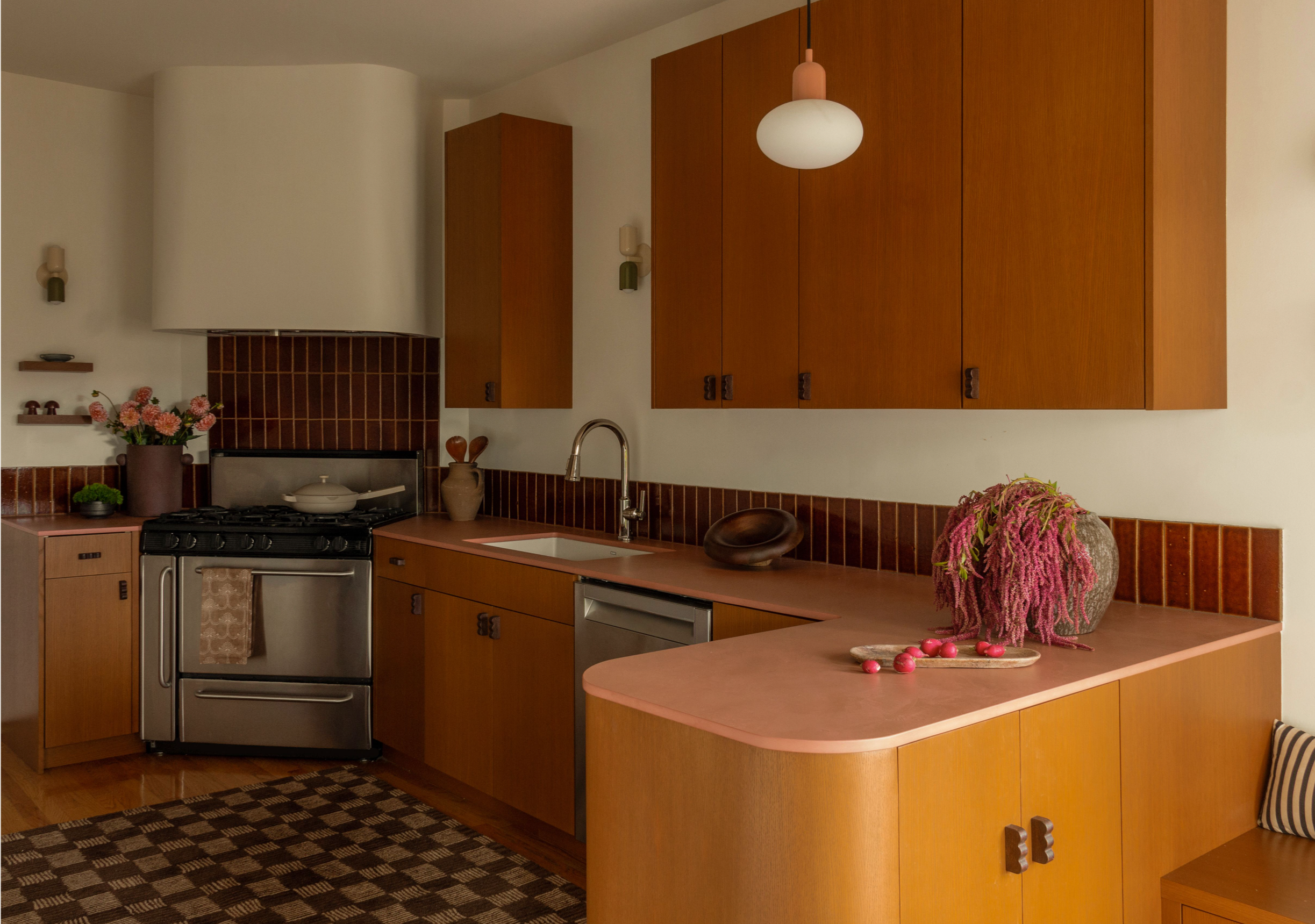 A kitchen with wooden cabinets, a stovetop, and various decorative items, including a large vase with pink and purple flowers and a plate of pink candies on the countertop.