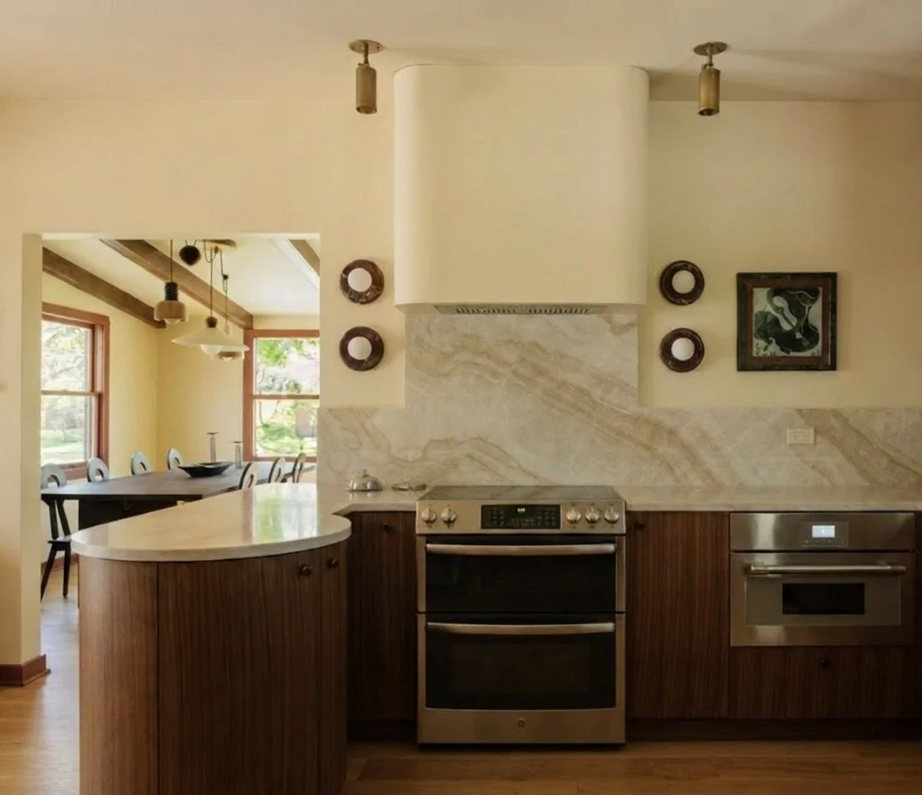 Kitchen with built-in oven, microwave, wooden cabinets, and a marble backsplash, adjacent to a dining room with large windows and a wooden table.