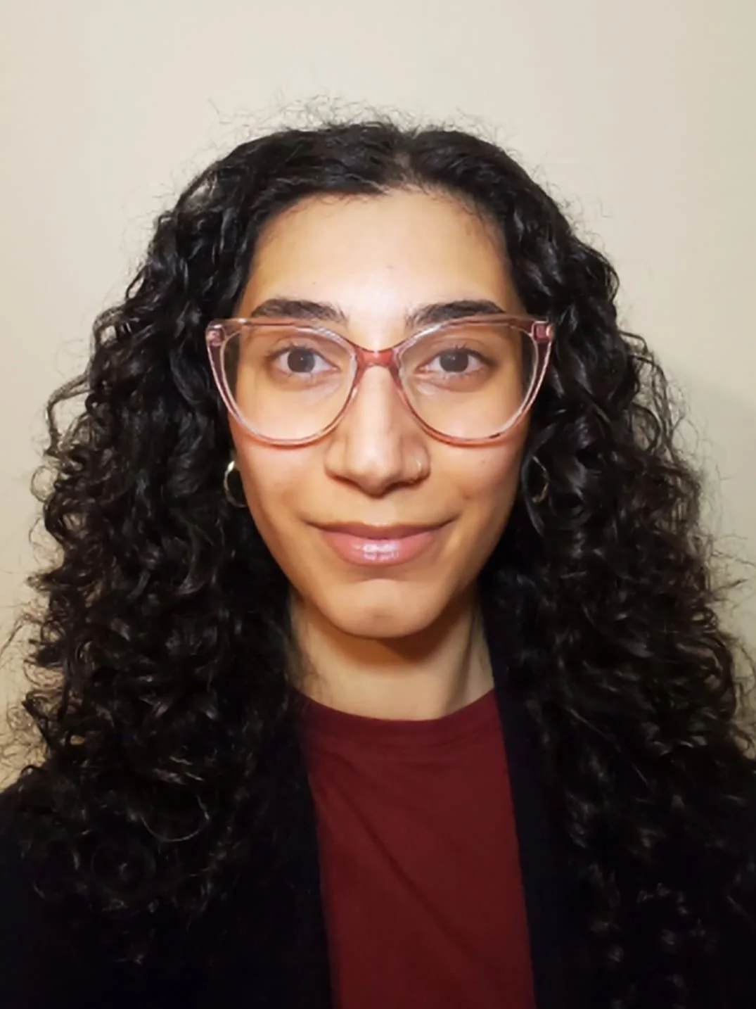 Middle Eastern woman with dark brown hair and pink glasses smiling at the camera.