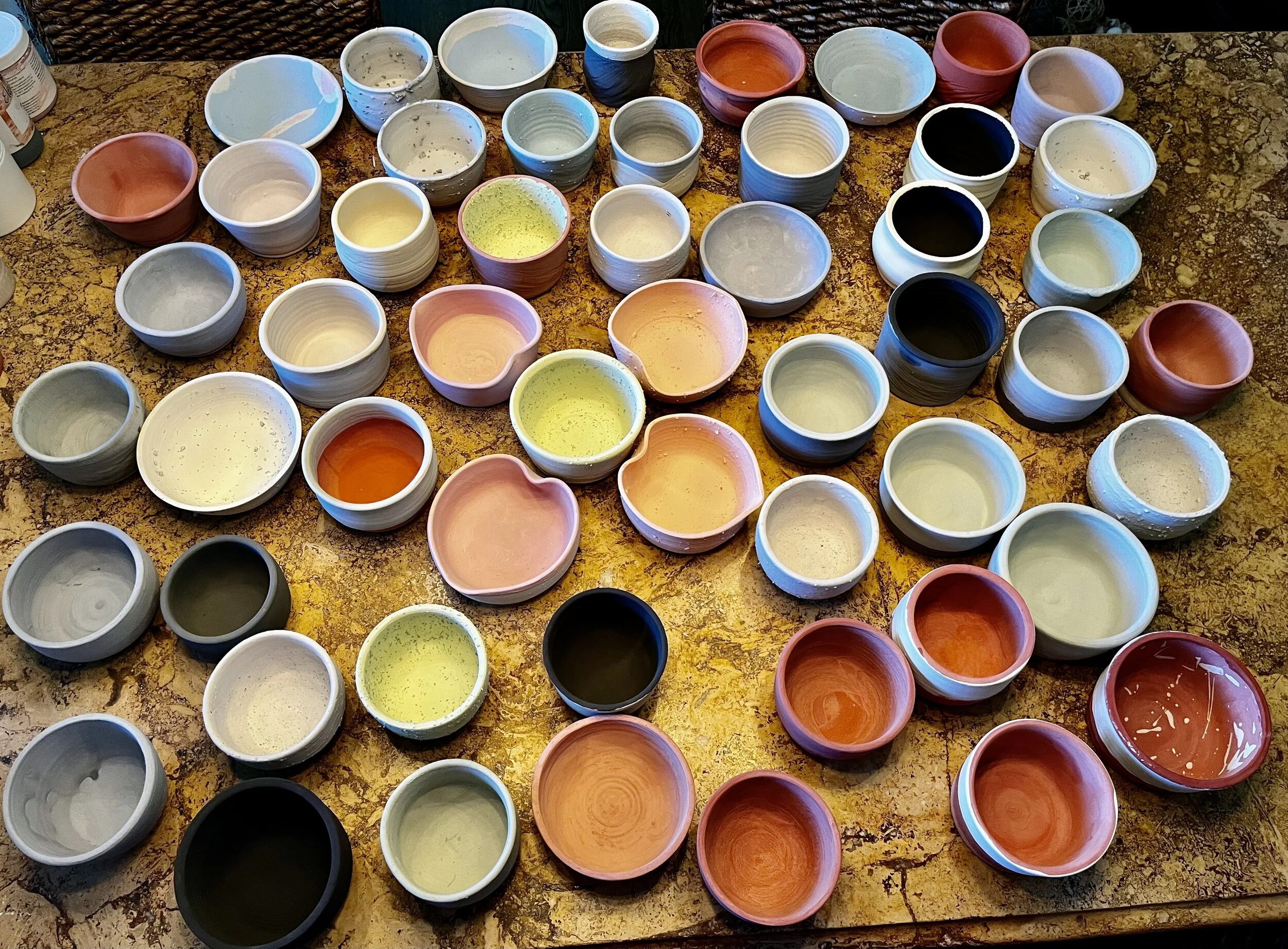 A collection of ceramic bowls in various colors and sizes, arranged on a marble surface.