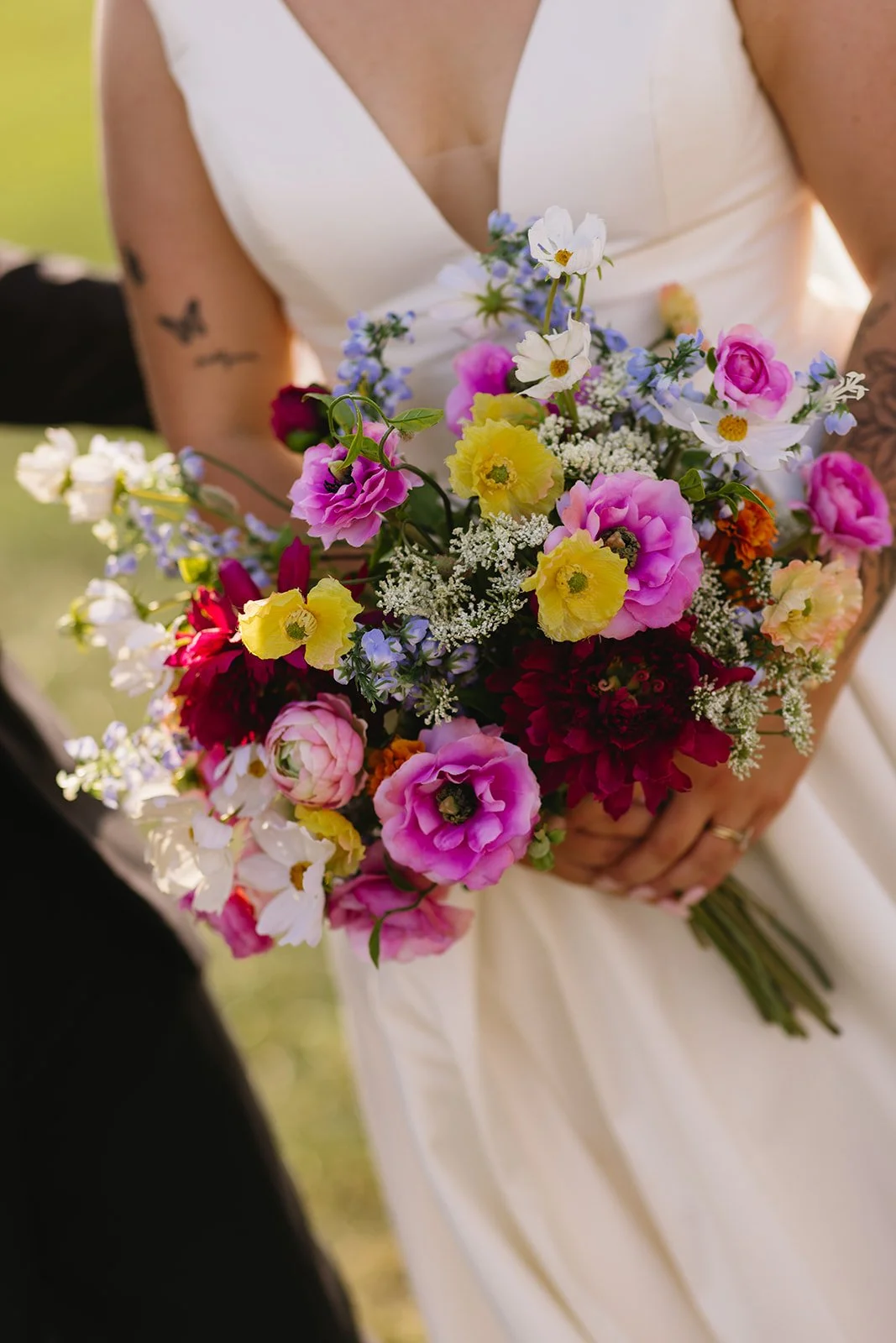 A woman in a white dress holding a colorful bouquet of various flowers, including pink, yellow, white, and dark red blossoms.