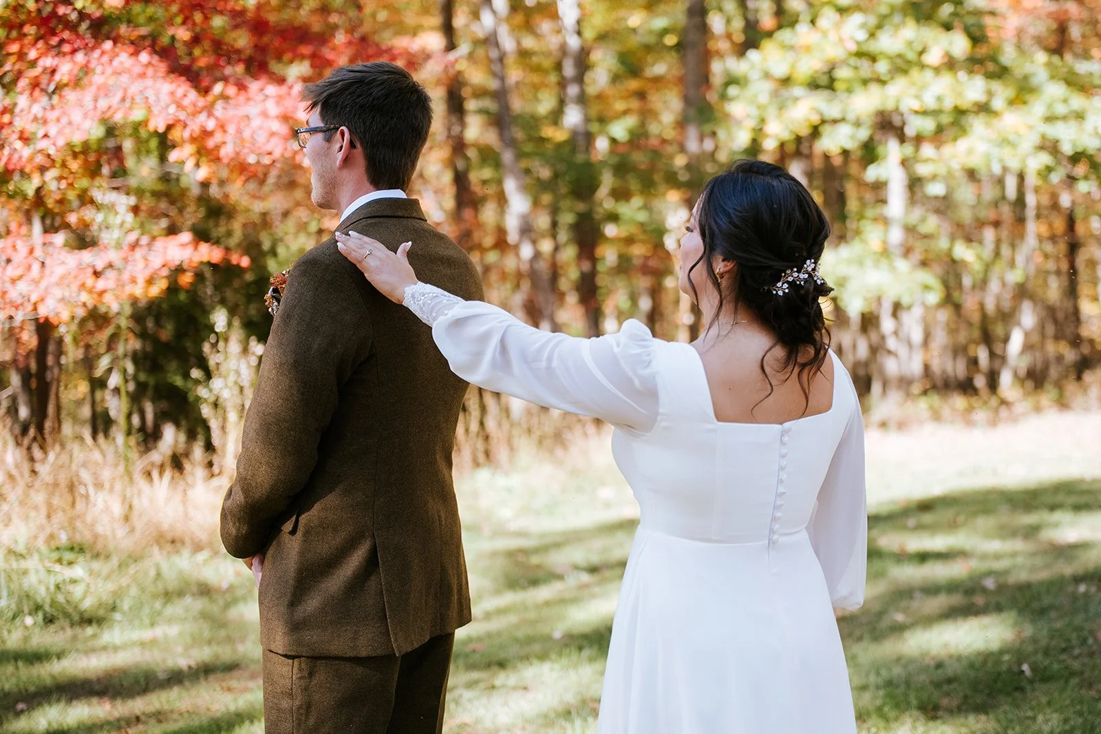 A bride and groom share a special moment outdoors during fall, with the bride touching the groom's shoulder. The scene features colorful autumn leaves in the background.