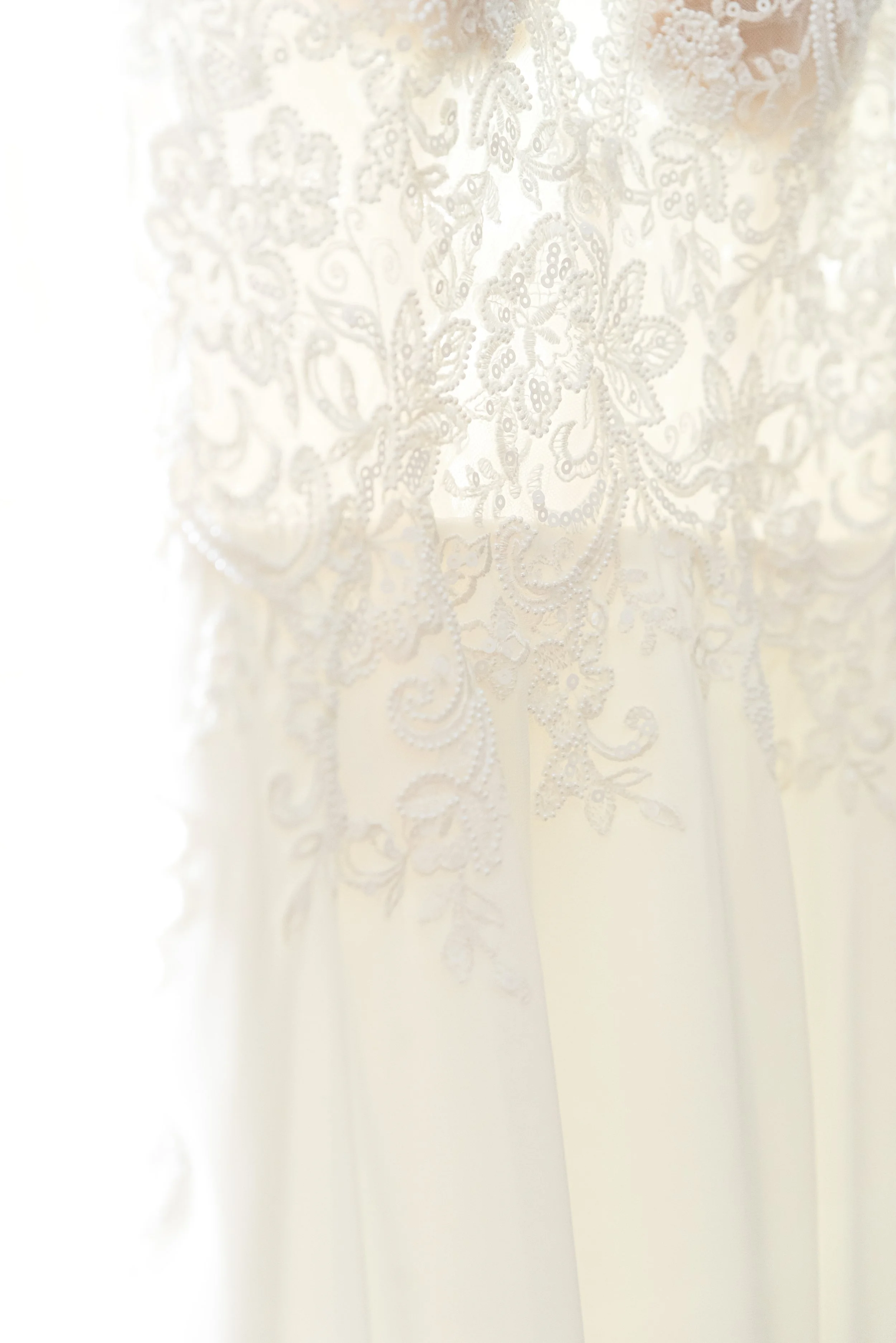 Close-up of a white wedding dress with intricate lace embroidery.