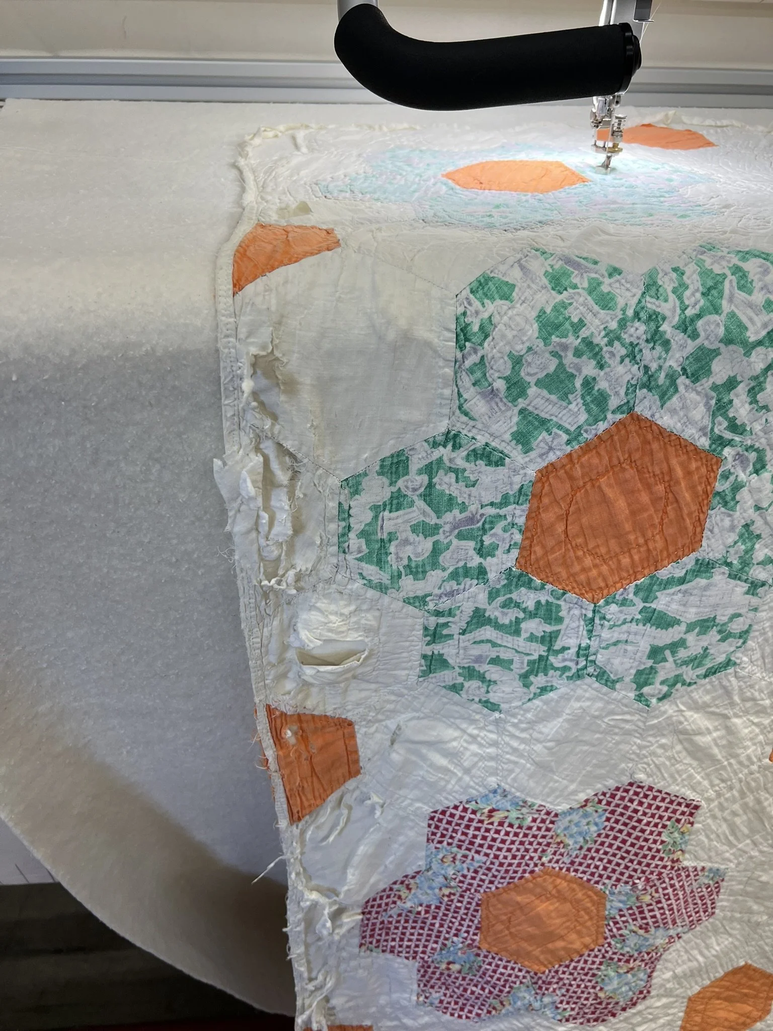 Close-up of a sewing machine stitching a quilt with colorful geometric patchwork designs.