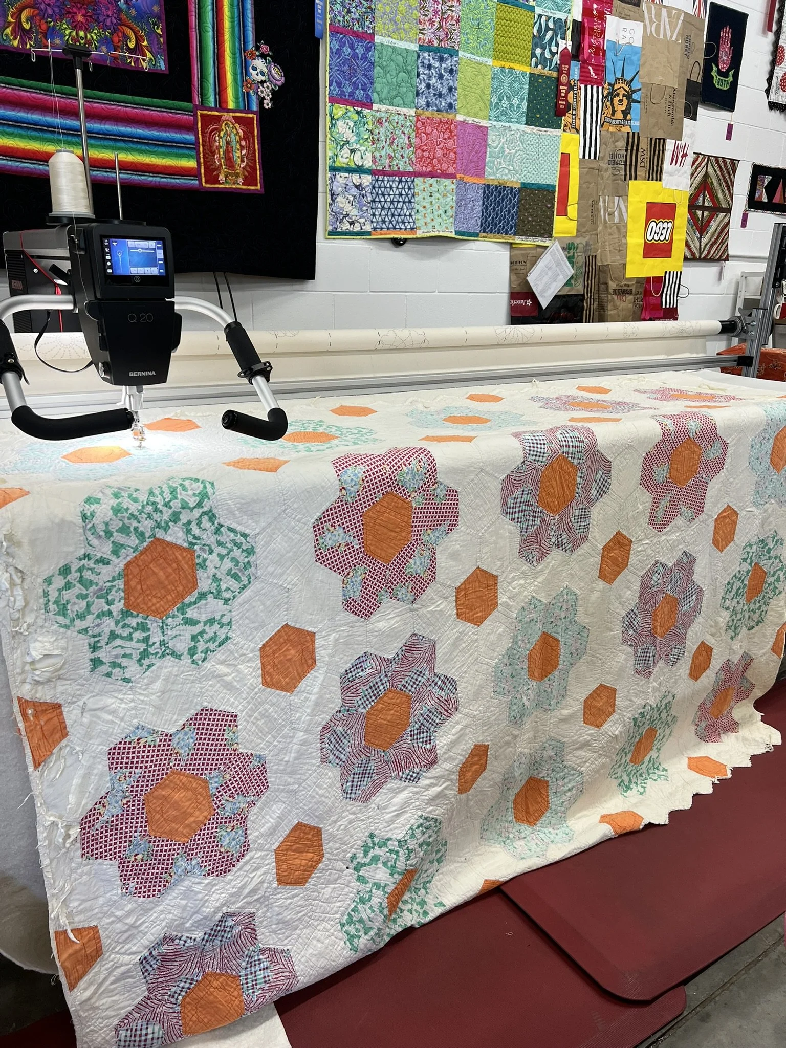 Colorful quilt with hexagon and floral patterns on a long arm quilting machine in a workshop.