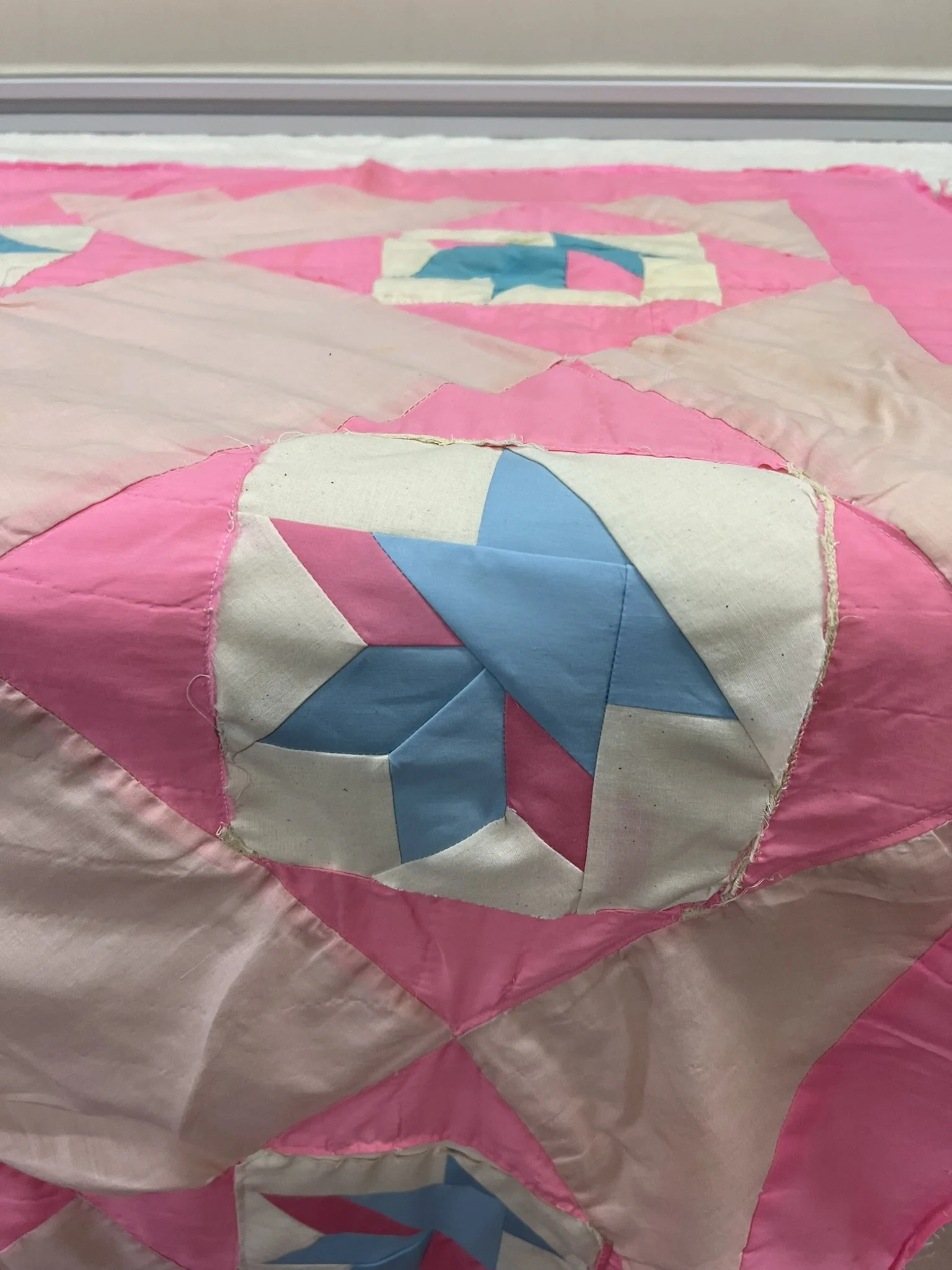 Close-up of a pink and white quilt with geometric star and heart patterns.