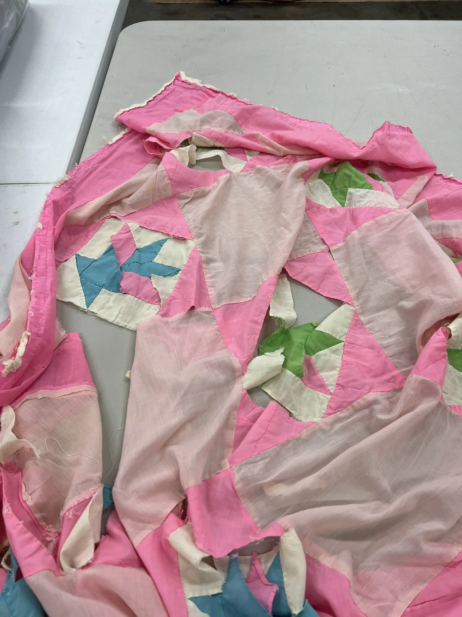 A pink quilt with various geometric patterns and green leaf designs, spread out on a gray surface.