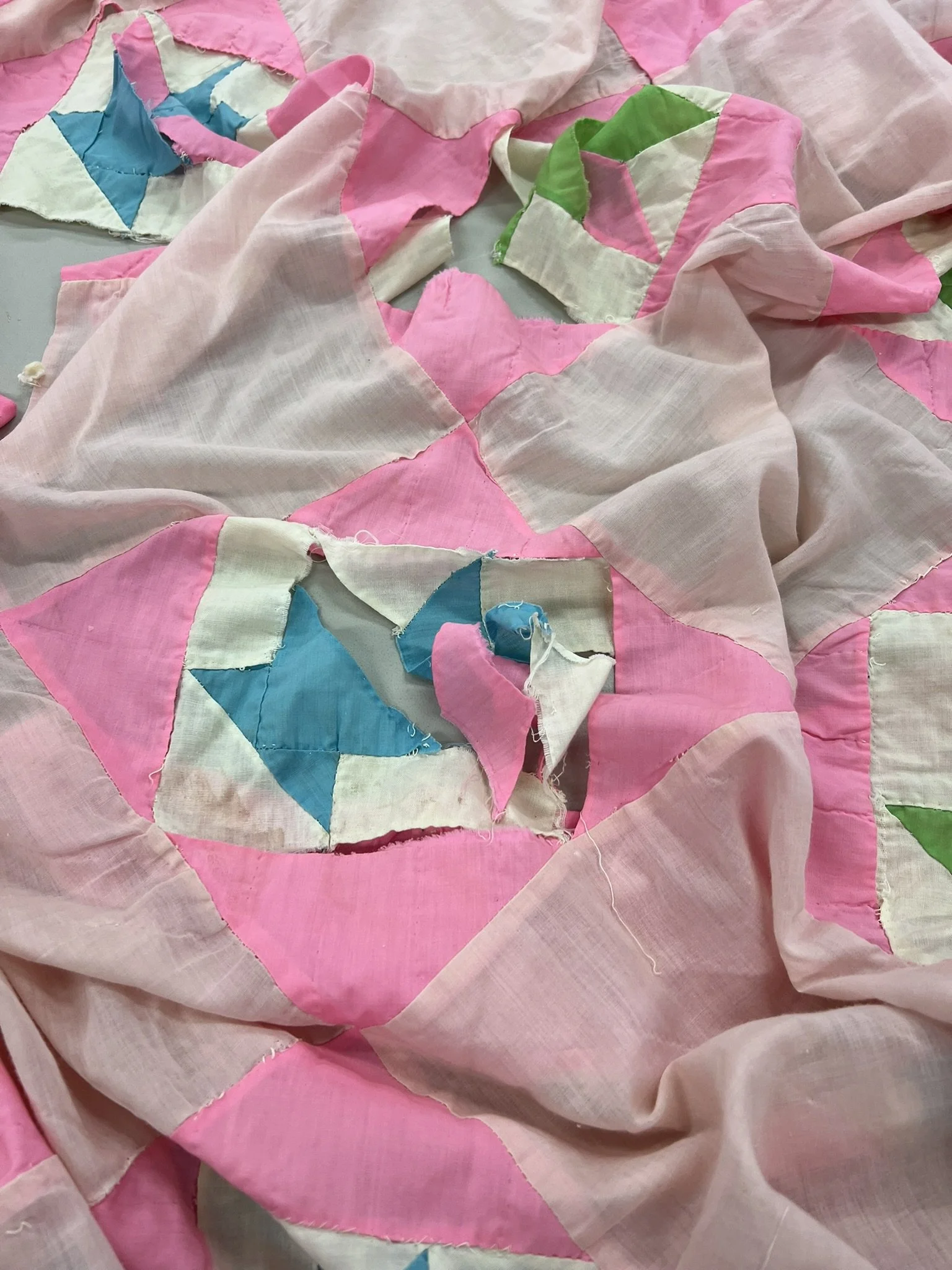 Close-up of a bandana quilt featuring pink, white, blue, and green fabric patches with star and color block patterns, some patches frayed and torn.