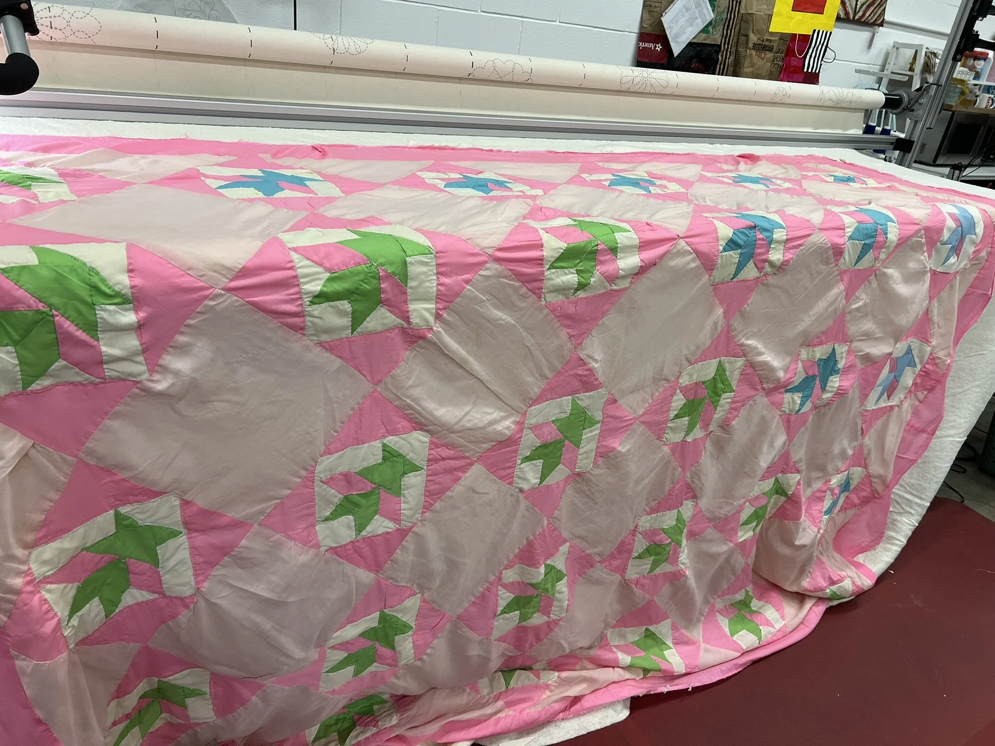 A pink and white quilt with green and blue star and leaf patterns draped over a table in a workshop setting.
