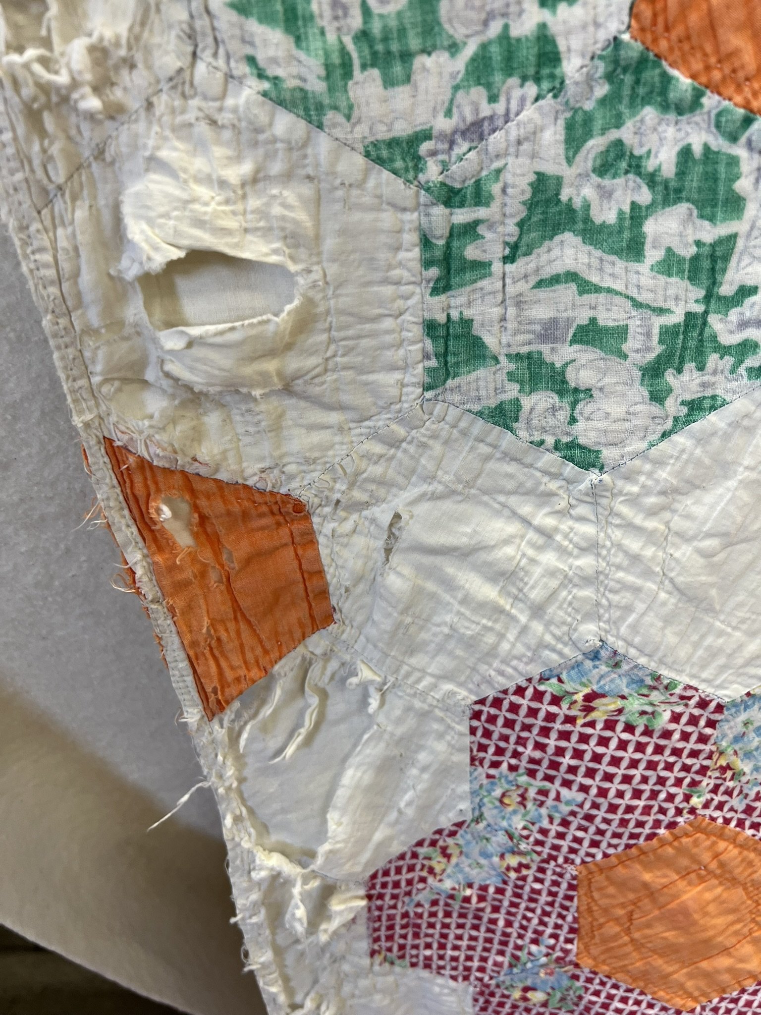 Close-up of a worn patchwork quilt with various colored fabric pieces, some torn or frayed, including green, orange, red, and white patterns.