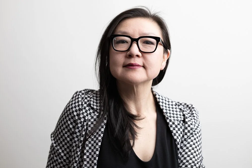 Asian woman with glasses and a suit smiling.