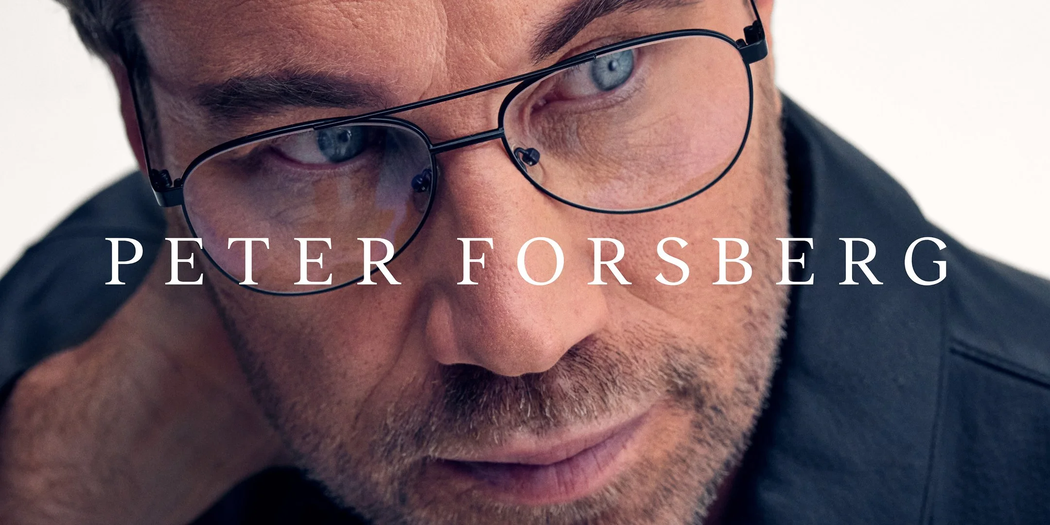 Närbild av en man med glasögon, med skägg och mörkt hår, som tittar nedåt.