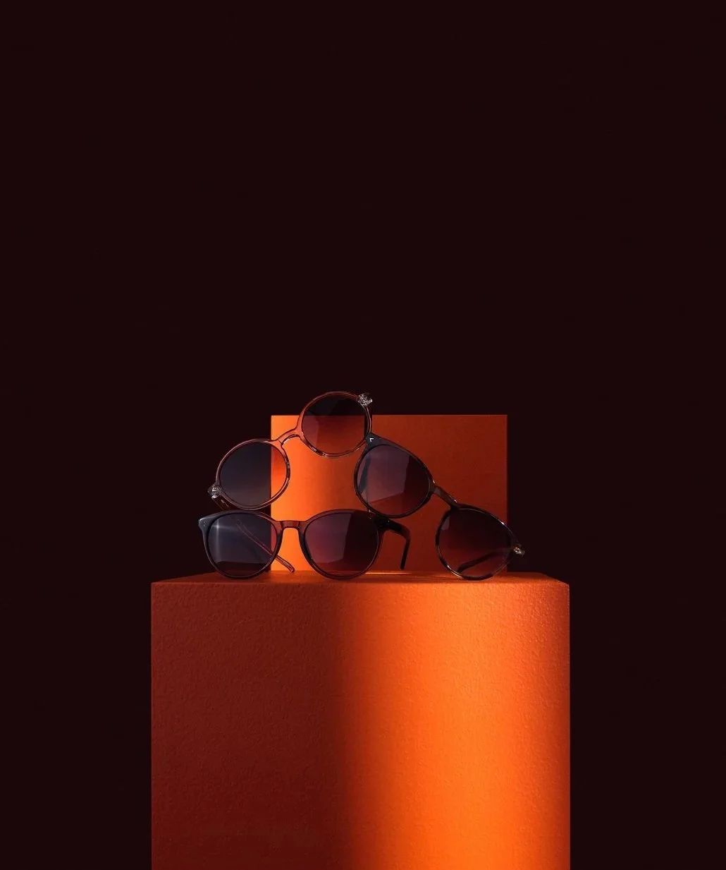 Tre par solglasögon med mörka glas, placerade på orangea pedestaler mot en mörk bakgrund.