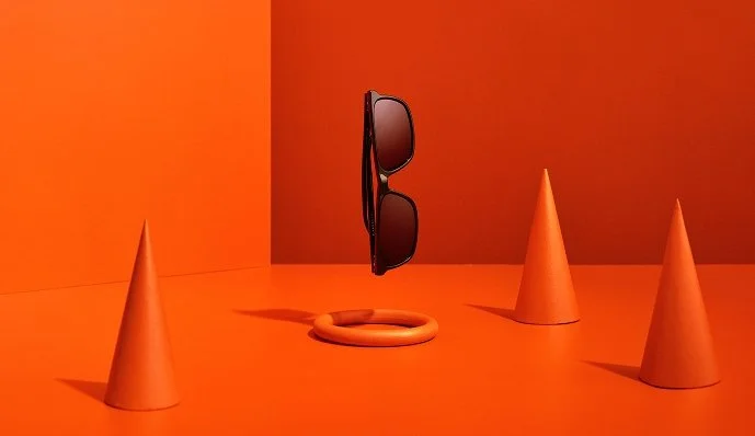 Solglasögon, ett hoprullat halsband och tre koner på en orange bakgrund.