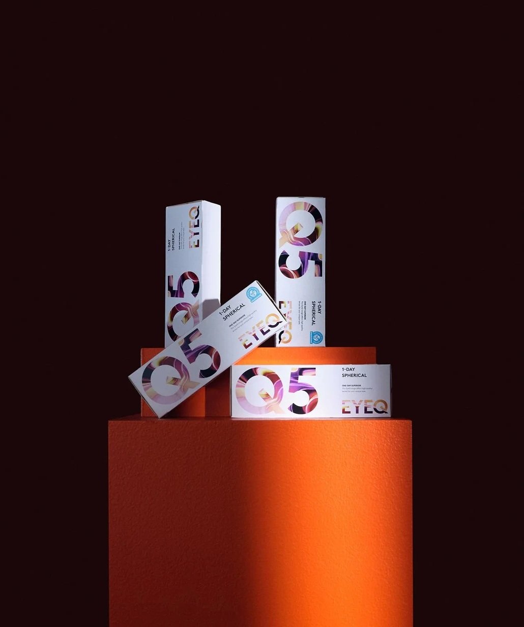 Flera förpackningar av EyeQ 1-dagssvirkel kontaktlinser på en orange pedestal, mot en mörk bakgrund.