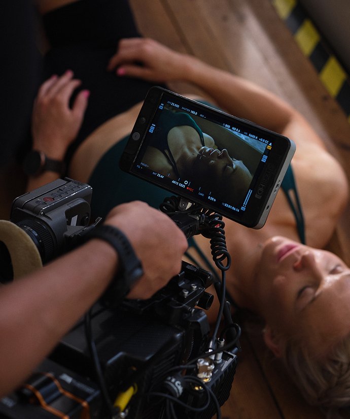 En person som filmar en kvinna som ligger på golvet med en kameramonitor.
