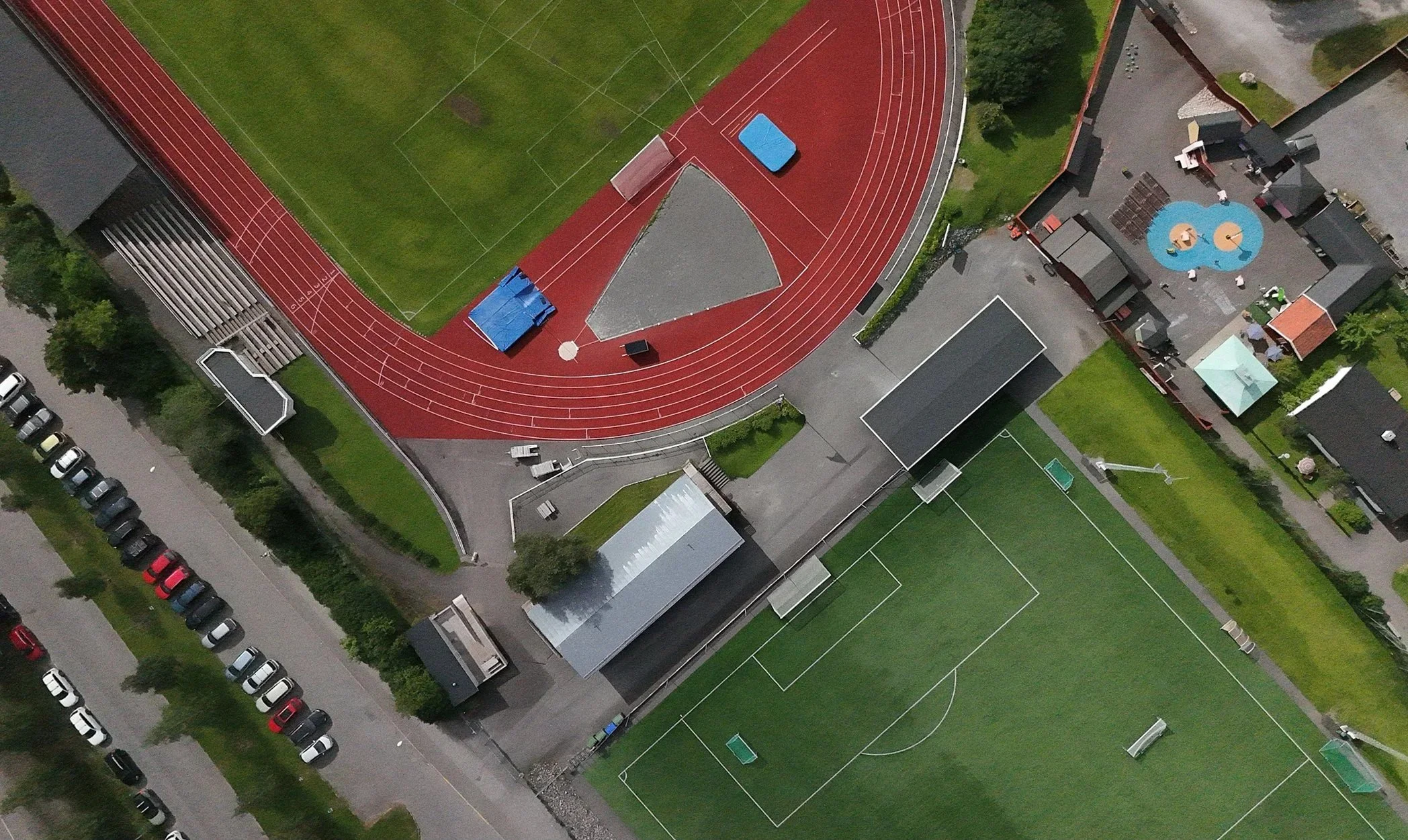 En ovanvåning av en idrottsplats med löparbanor, fotbollsplan och omgivande byggnader samt parkeringsplatser.