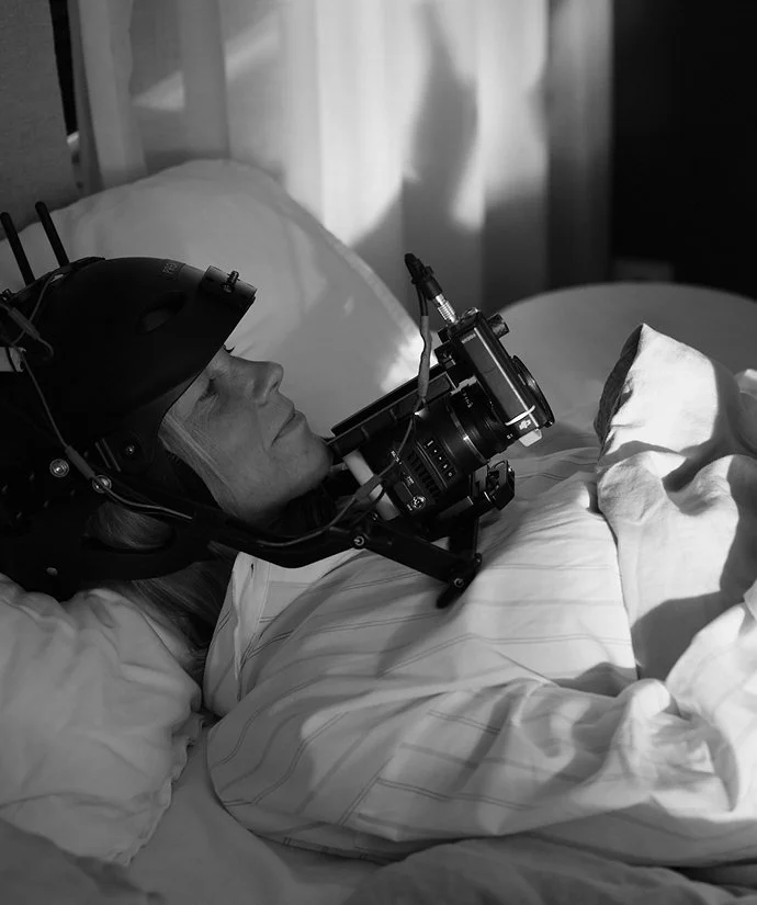 Kvinna ligger i säng med VR-headset och kamerautrustning.