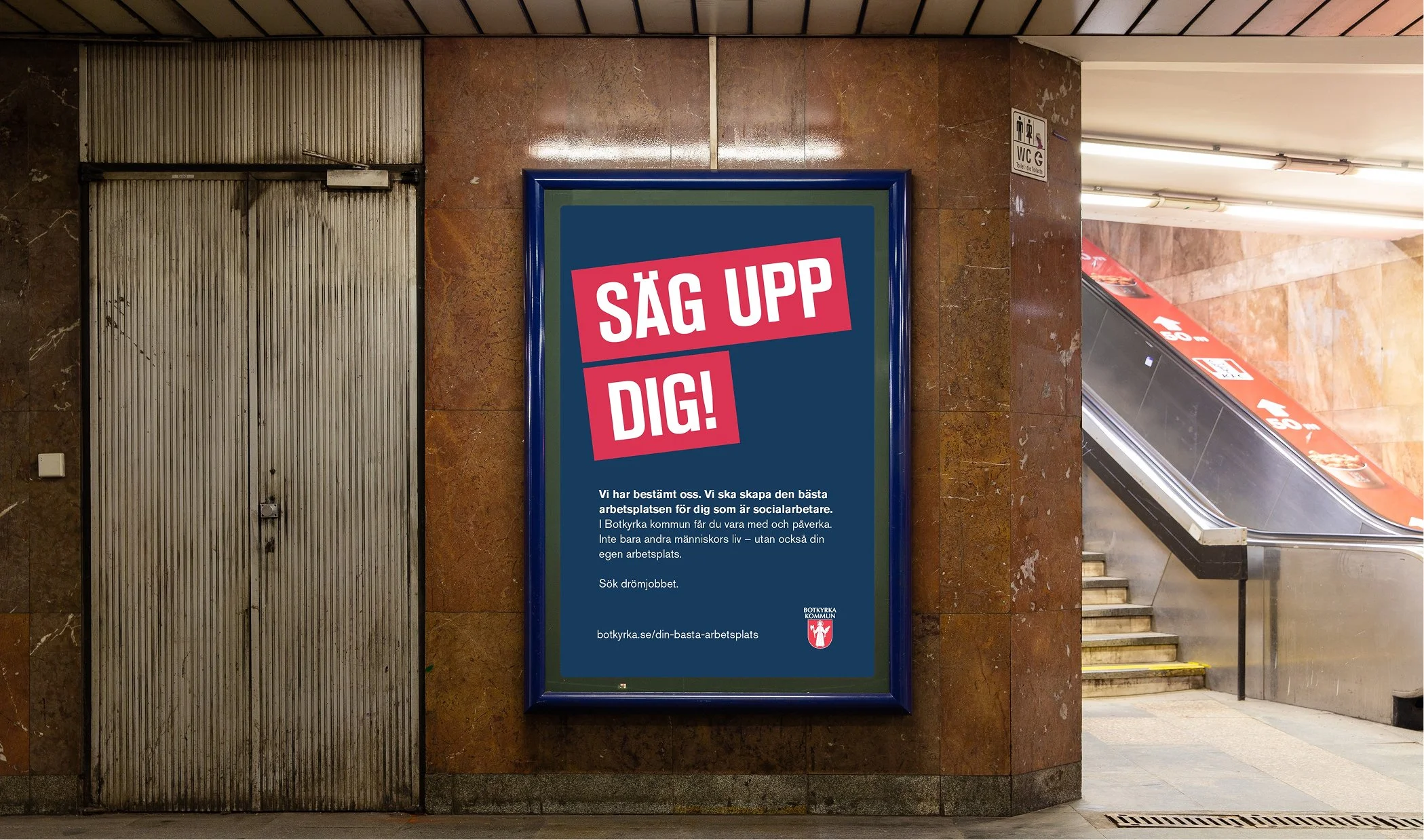 En annonsvägg i en underjordisk station med texten 'SÄG UPP DIG!' i stora röda och vita bokstäver. Nedanför finns ytterligare information i mindre text om att skapa den bästa arbetsplatsen för socialarbetare i Botkyrka kommun.