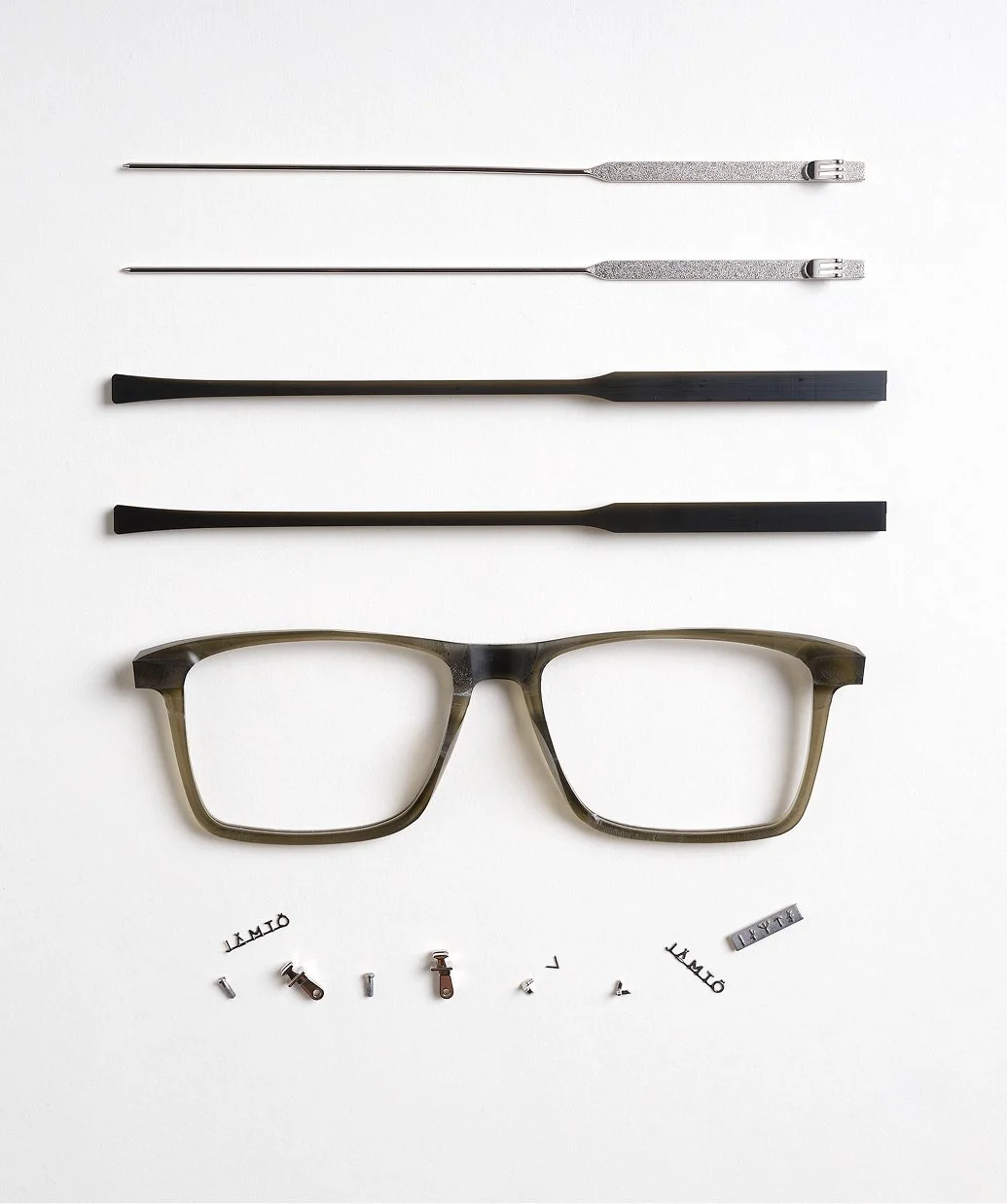 Syntetiska ögonbrynstryck, två pincetter, en spatel, en par glasögon, samt små delar och etiketter som används för glasögontillverkning eller justering.