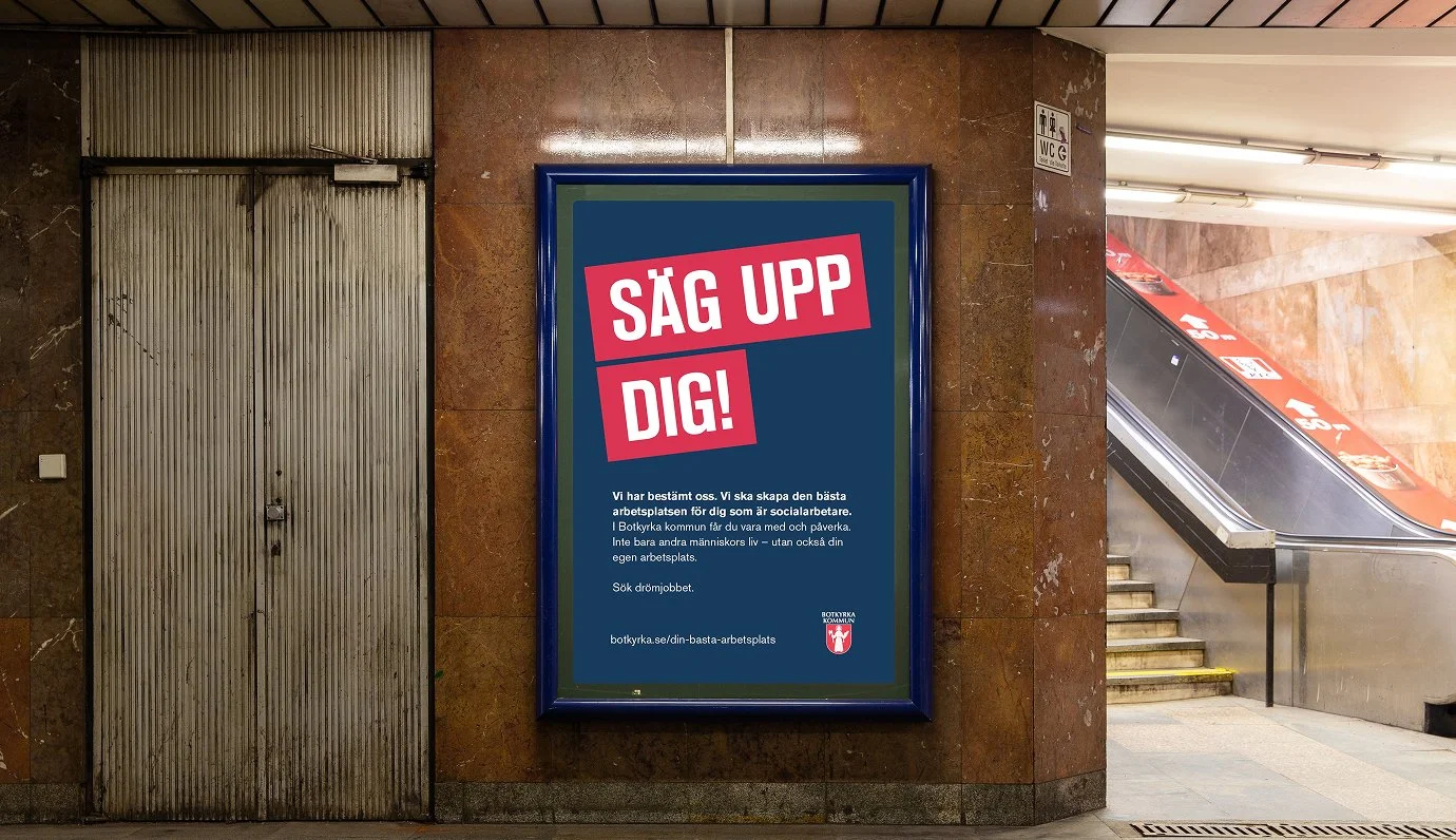 Affisch i tunnelbanestation med texten 'SÄG UPP DIG!' och information om att skapa den bästa arbetsplatsen för socialarbetare i Botkyrka kommun.
