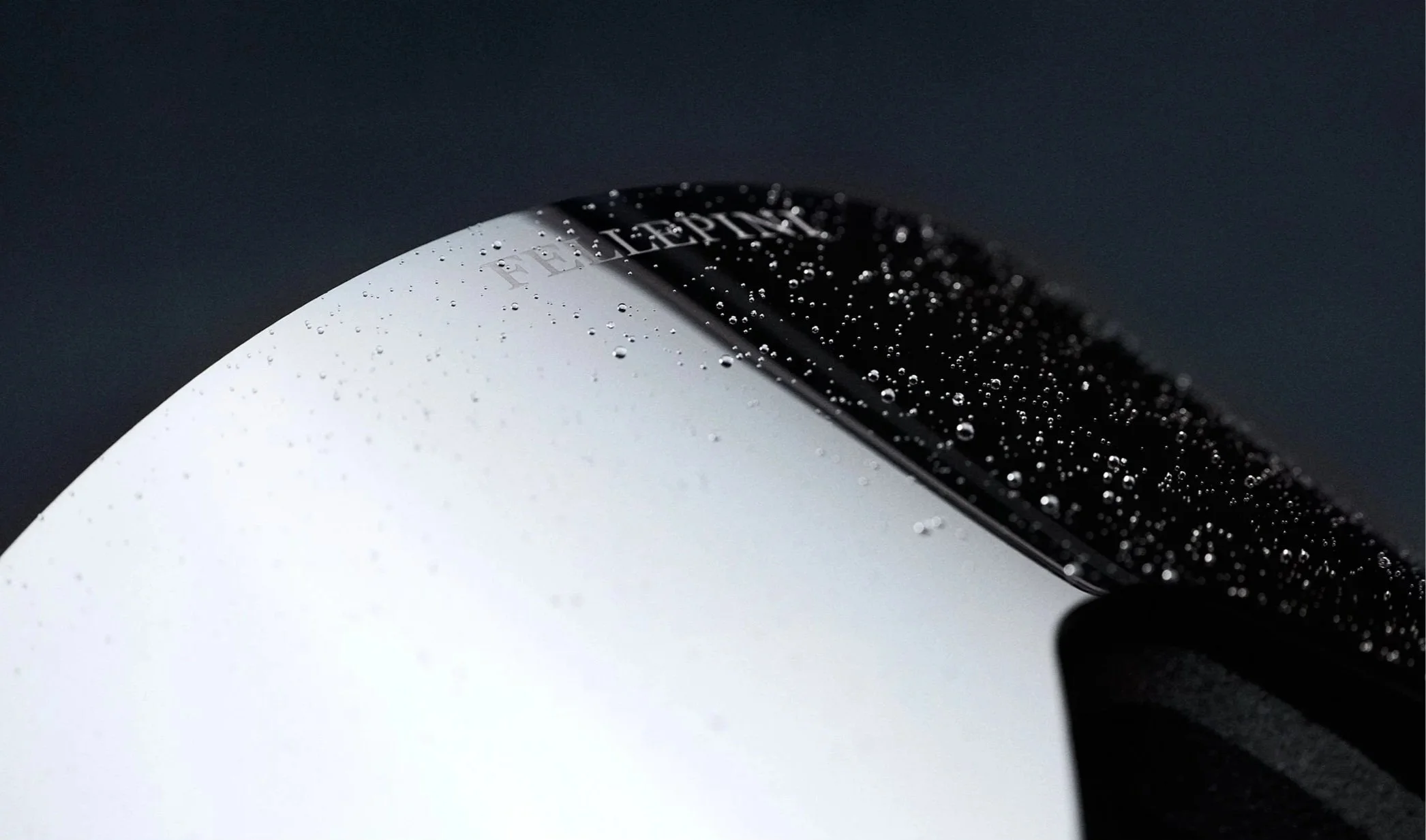 Närbild av en vit och svart kaffekopp med vattenpärlor på ytan, mot en mörk bakgrund.