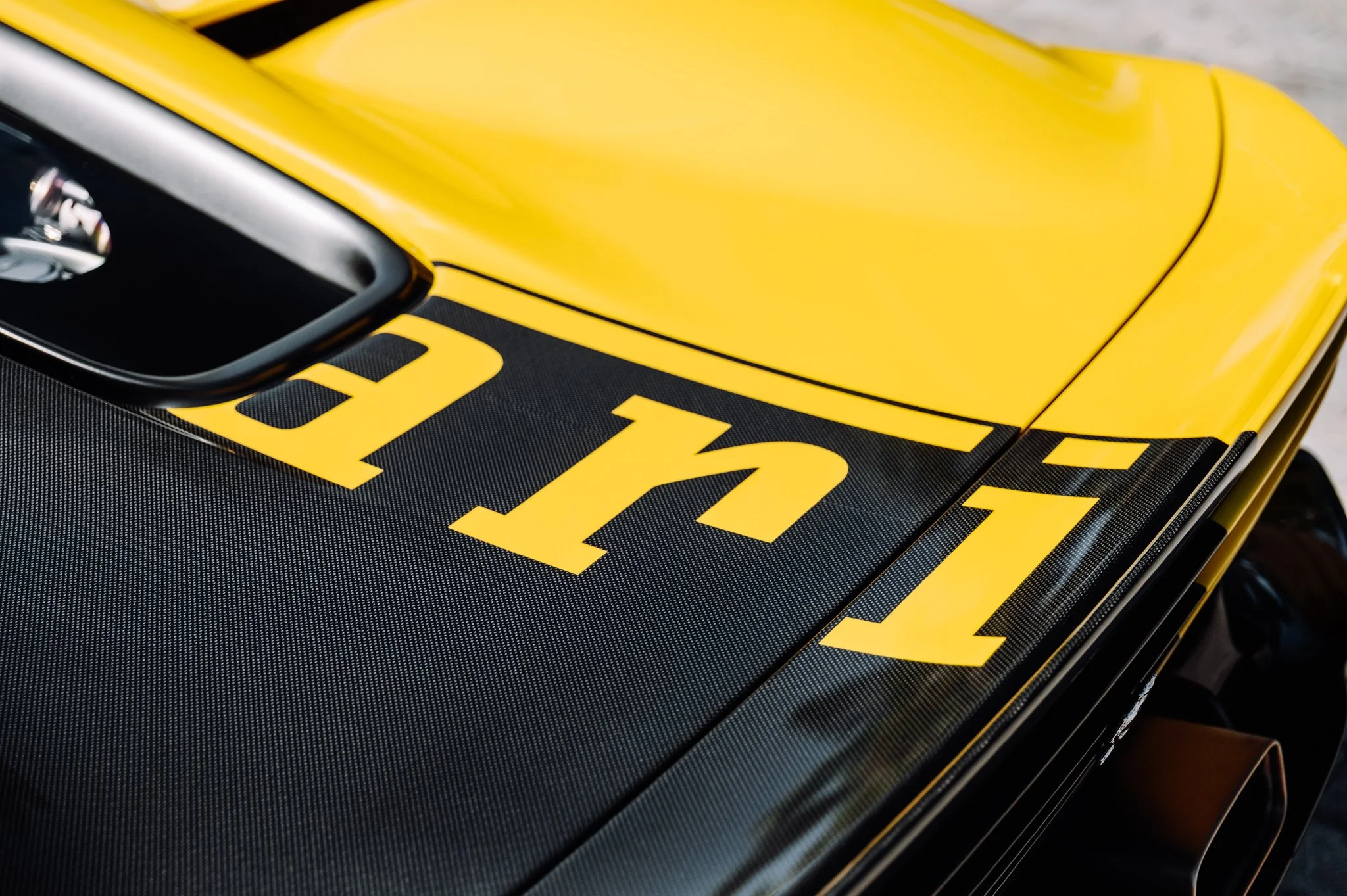 Close-up of a yellow race car with black accents and a large black number on the hood.