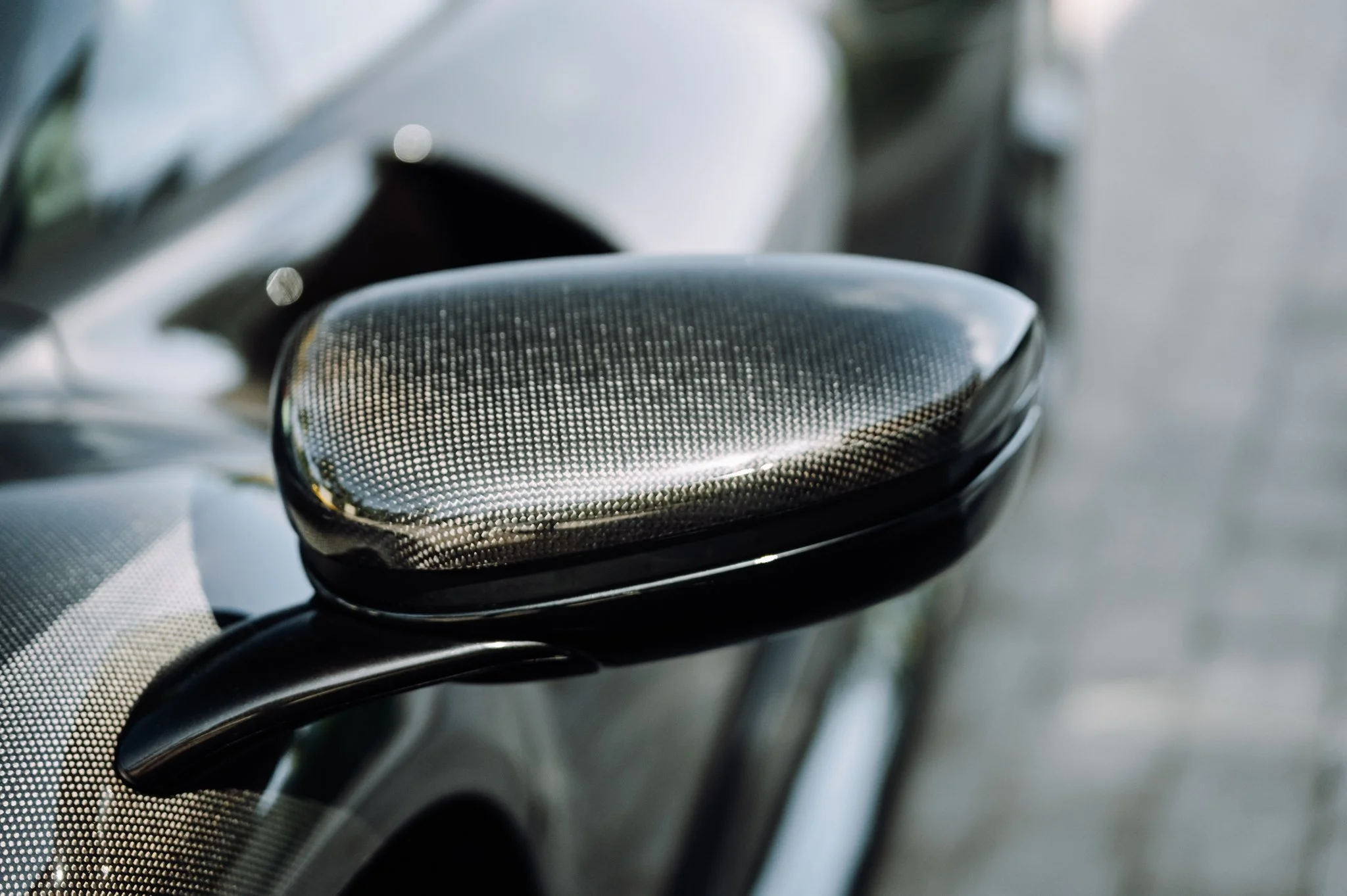 Close-up of a carbon fiber motorcycle side mirror with a blurred background.