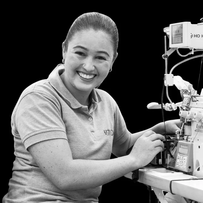 Close-up of a man with curly dark hair, clear glasses, a nose ring, a beard, wearing a dark green sweater, smiling slightly, indoors with a blurred background.
