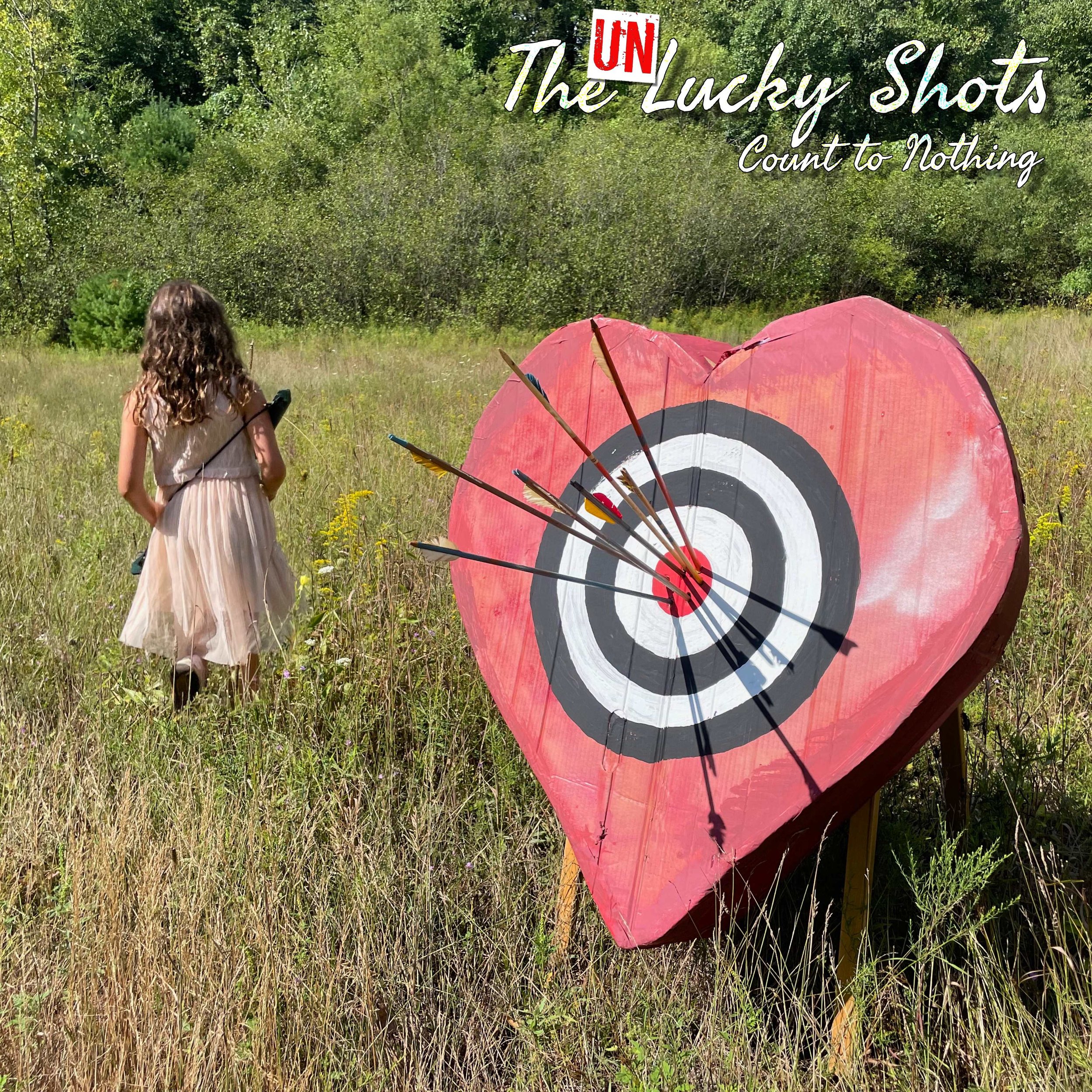 A girl with curly hair wearing a beige dress walking away from a large, heart-shaped archery target with arrows stuck in its center in a grassy field with trees in the background.