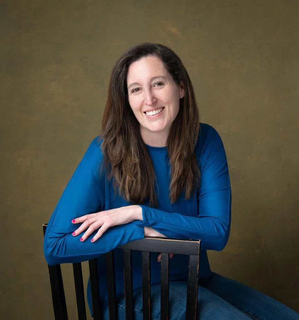Rachel Davila, brunette wearing blue shirt and blue jeans propped on a chair