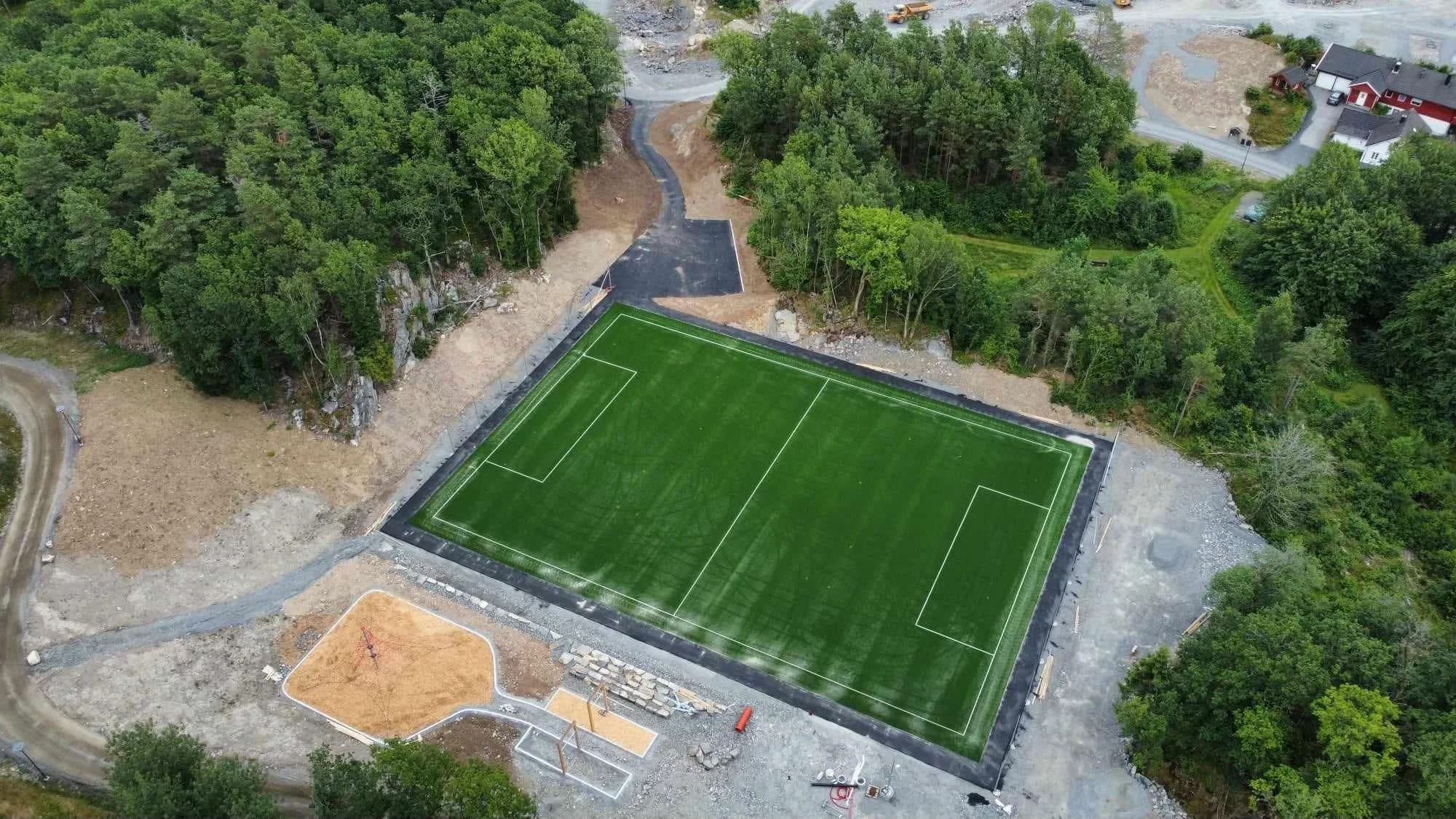Aerial view av en tennisbane under bygging, omgitt av skoger og et lite boligområde.