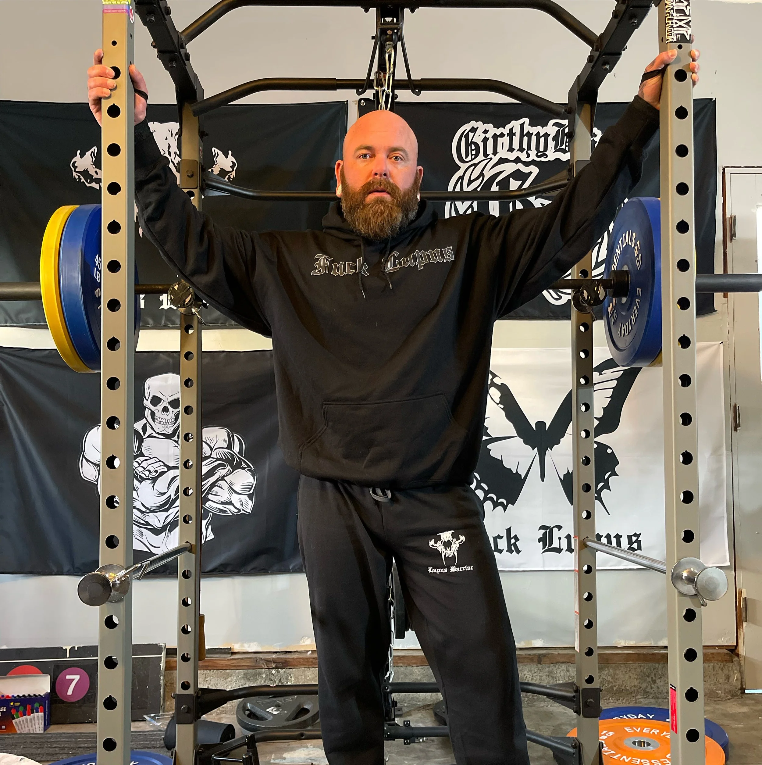 A man with a beard lifting a barbell with weights inside a power rack at a gym.