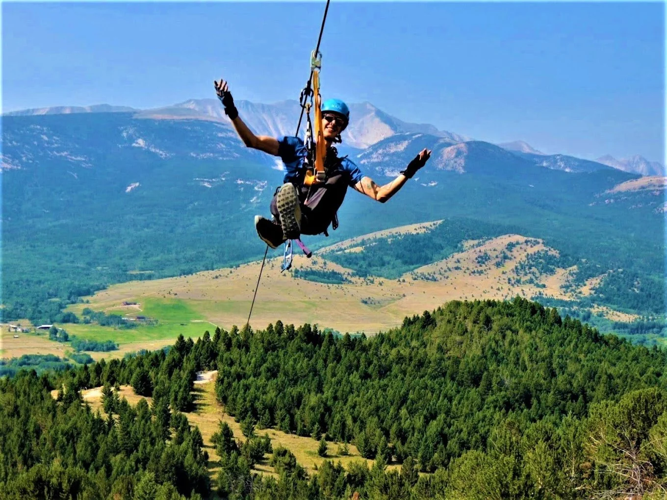 Person bungee jumping over a lush green forested area with mountains in the background on a clear day.