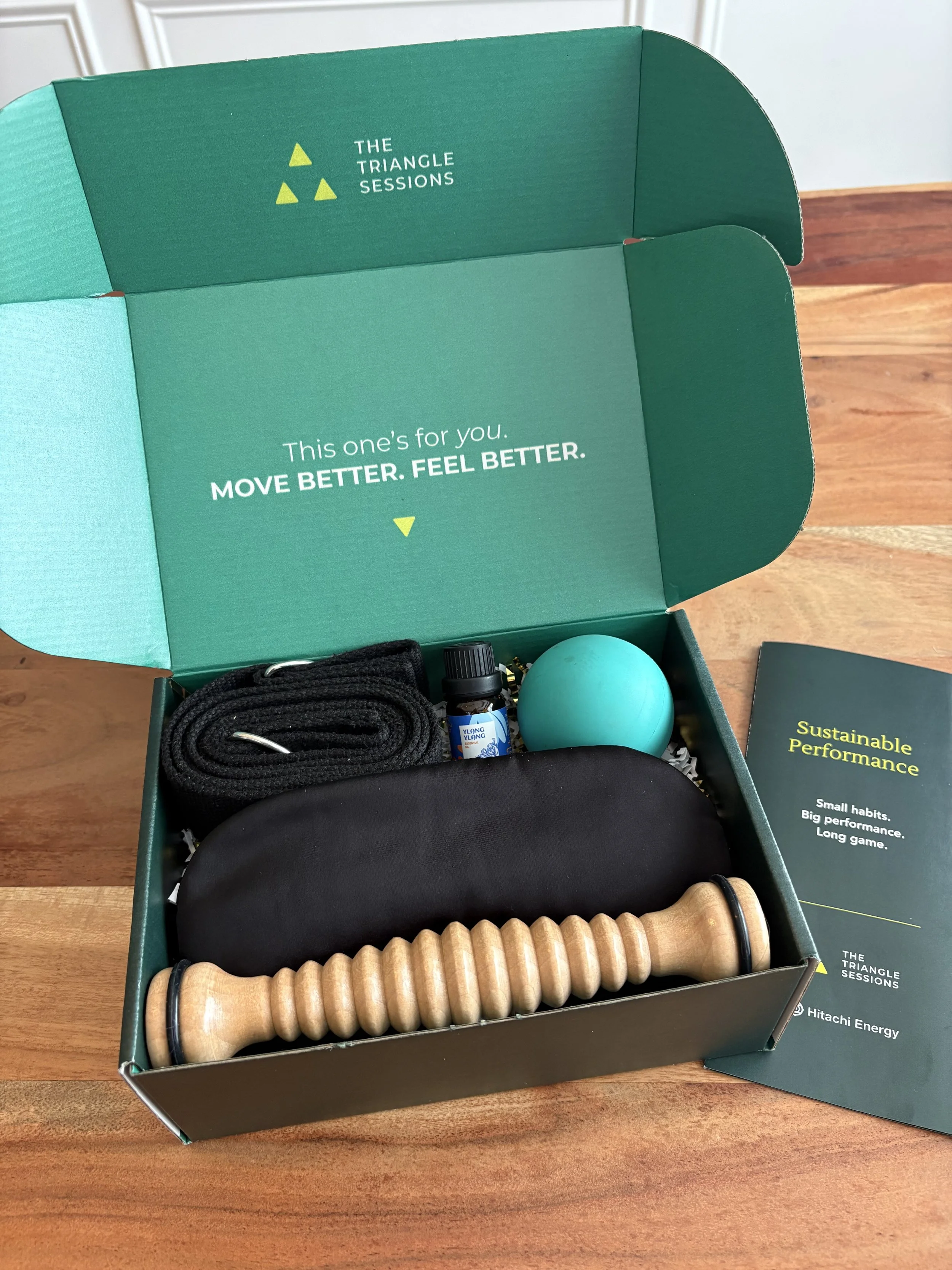 A Performance Recovery Kit containing a coiled black rope, a small dark bottle, a light blue exercise ball, a black eye mask, a wooden massage roller, and a pamphlet titled 'Sustainable Performance'.