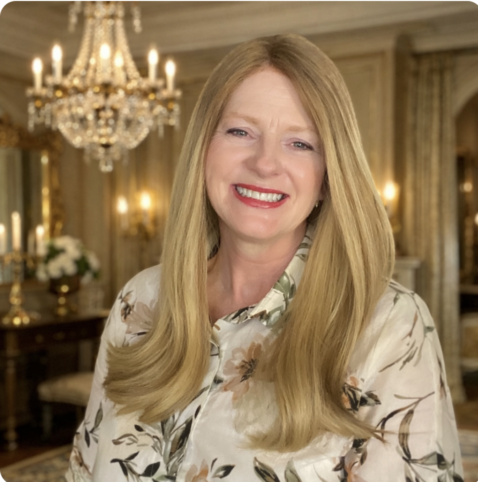 A woman with long blonde hair and red lipstick smiling in a luxurious room with a chandelier and ornate decor.