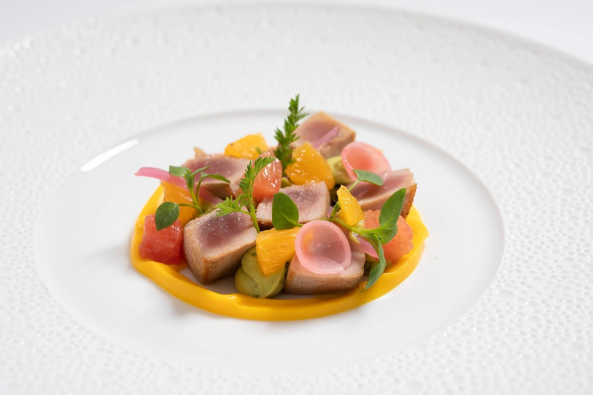 Assiette de tartare de poisson avec des agrumes, des microgreens et des crisps de légumes, présentée élégamment sur une assiette blanche.